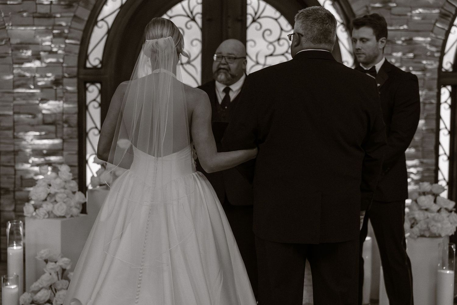 A formal wedding ceremony taking place under a stone archway with guests watching the couple's special moment.