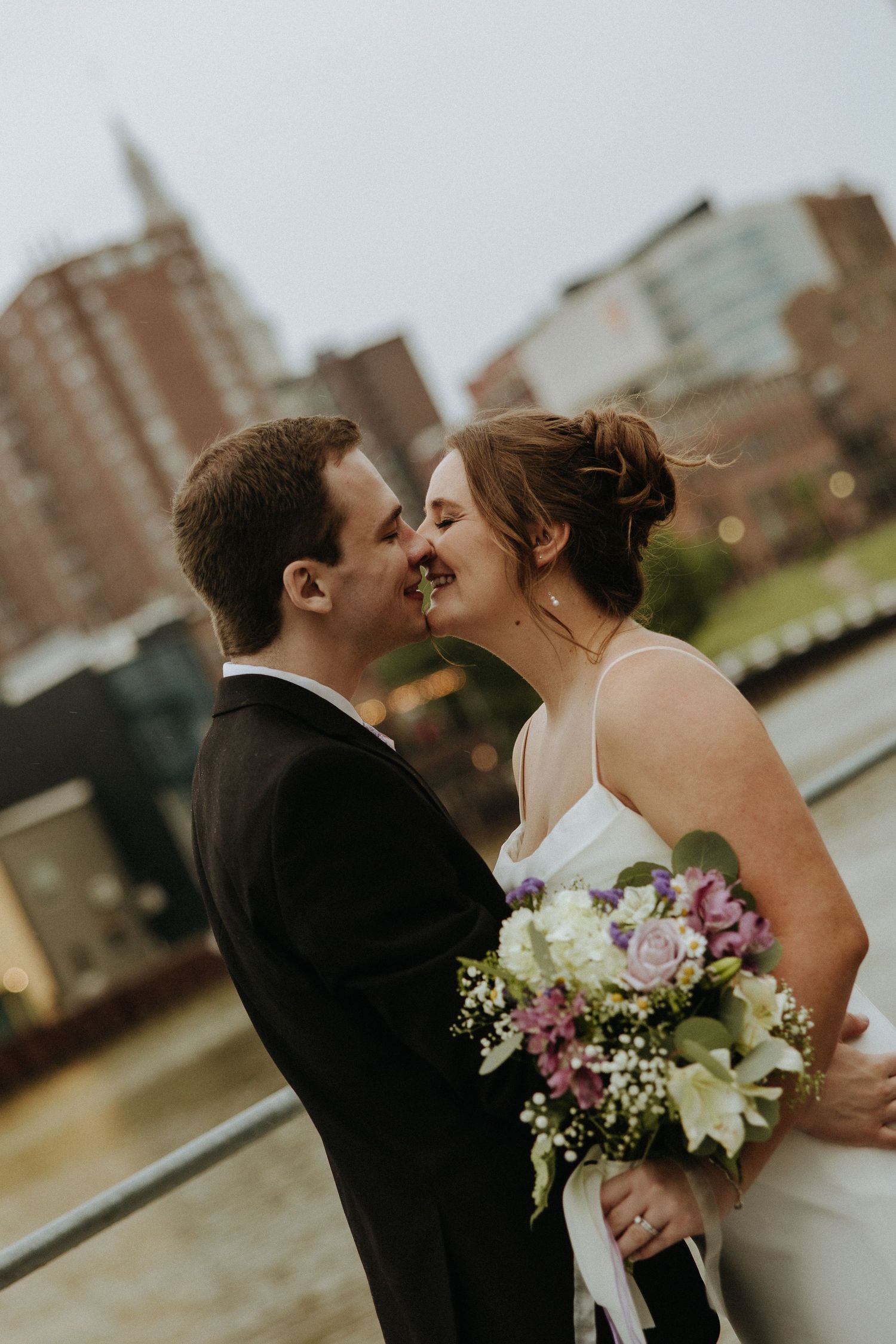 Wedding couple embracing with city skyline in background during sunset.
