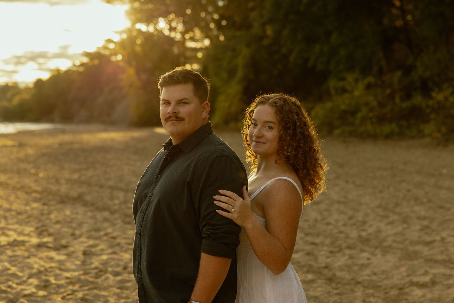 A couple shares a romantic moment at sunset on a beach with golden light illuminating the scene.