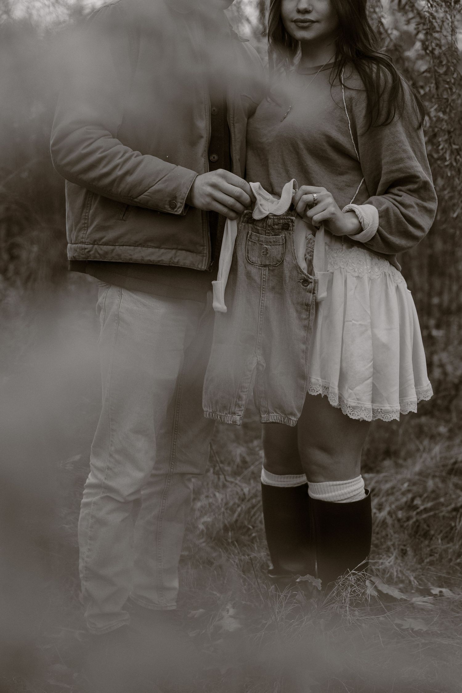A moody black and white photograph showing two people holding hands in casual clothing with a dreamy foggy effect.