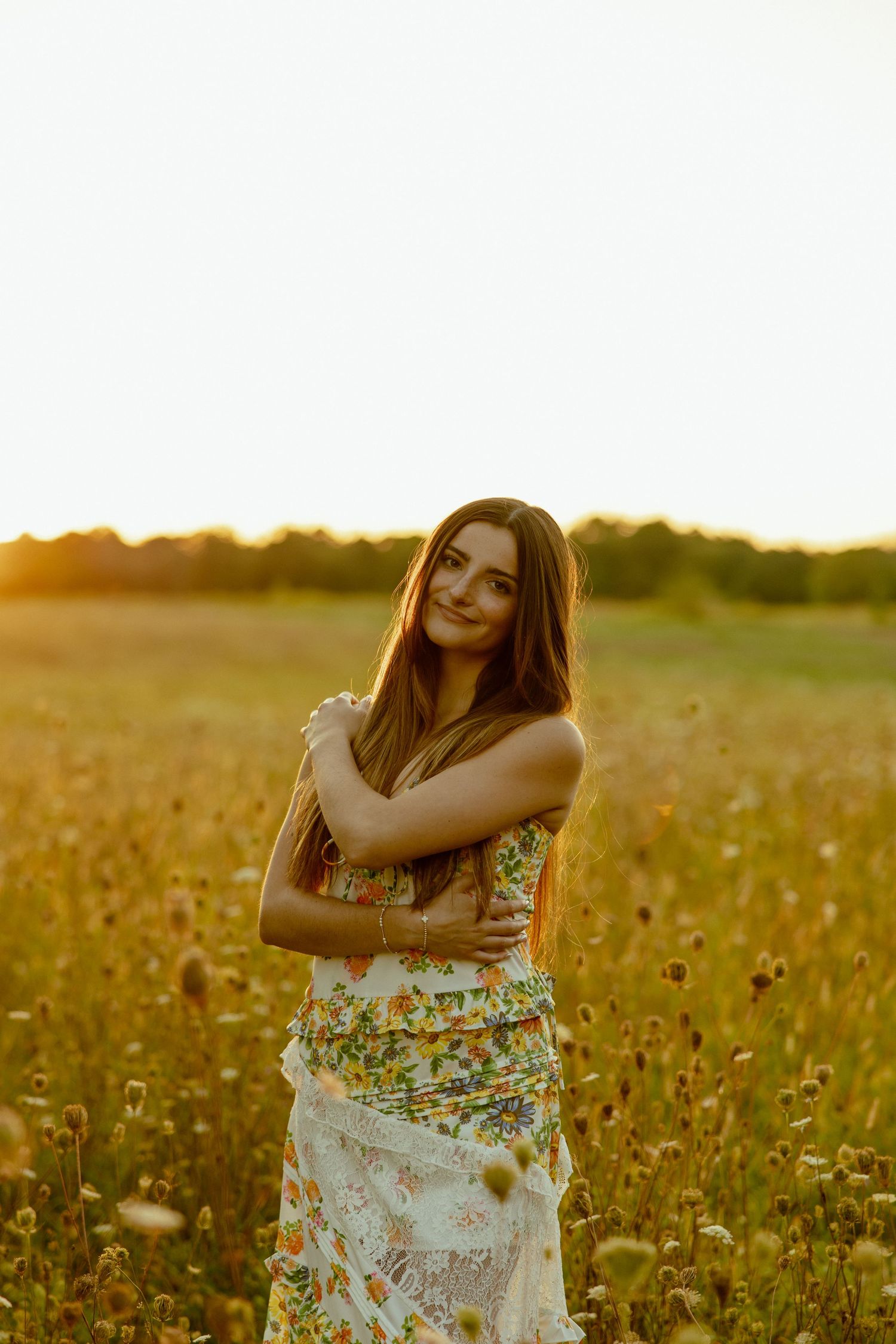A person in a floral dress stands in a golden wildflower field at sunset.