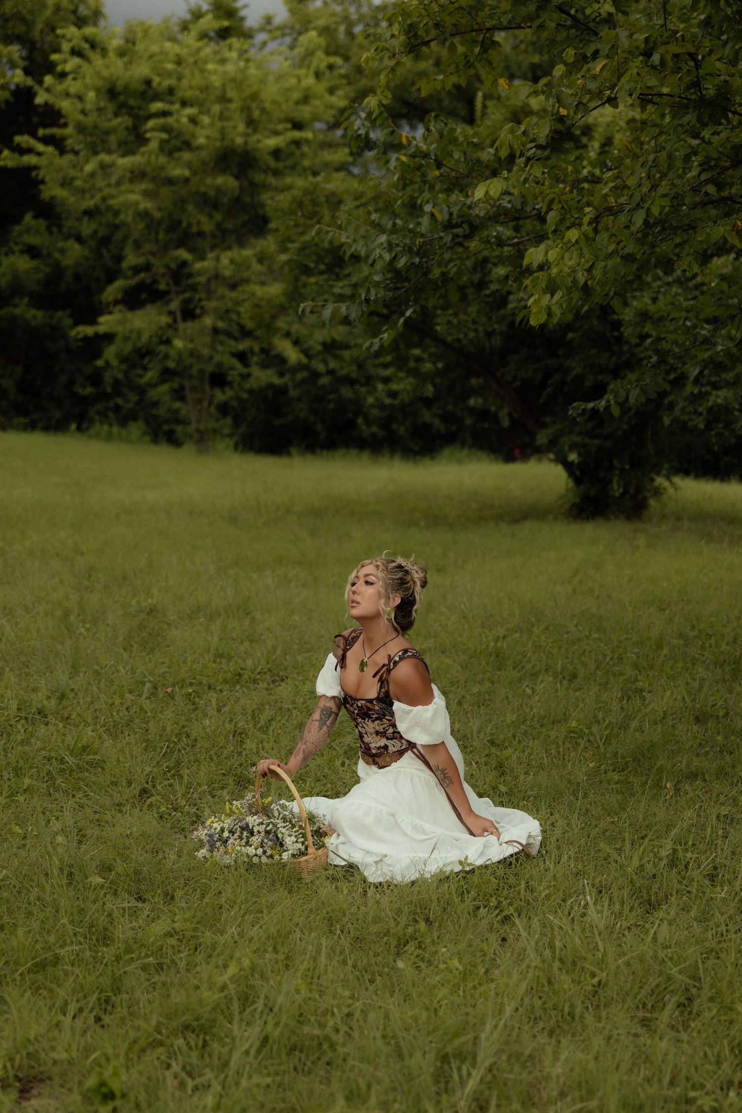 A woman in a white dress reclines gracefully in a sunlit meadow surrounded by lush greenery.