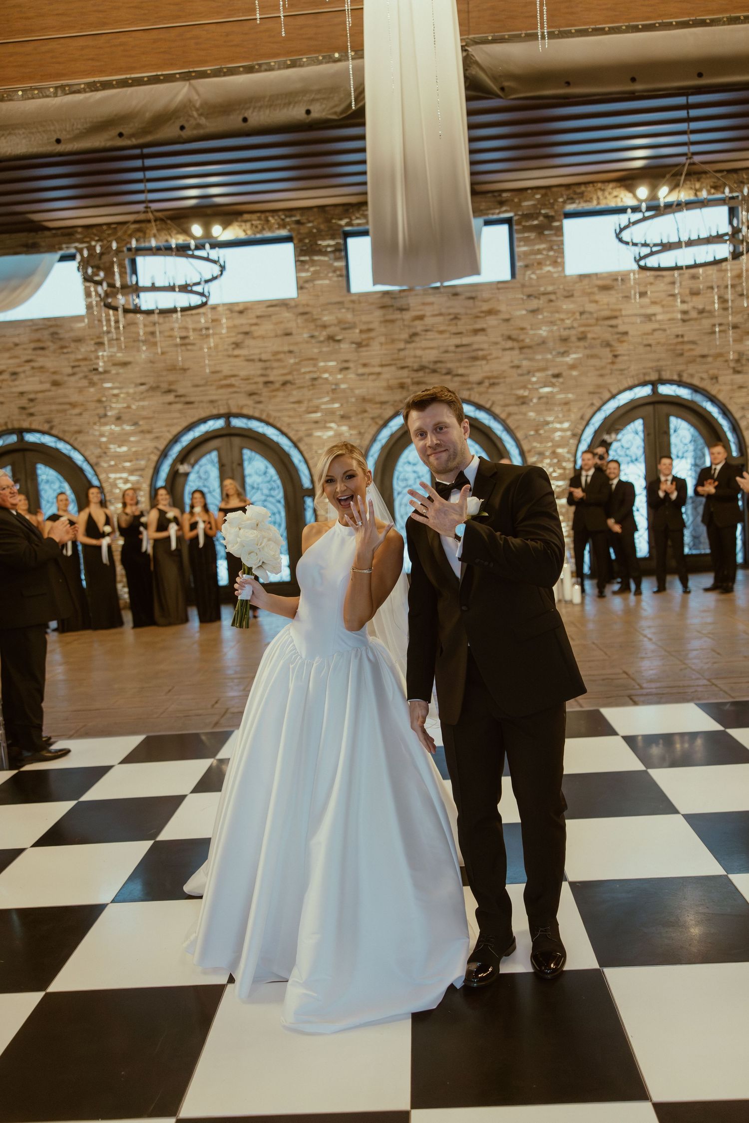 Wedding celebration on a black and white checkered dance floor with stone walls and arched windows.