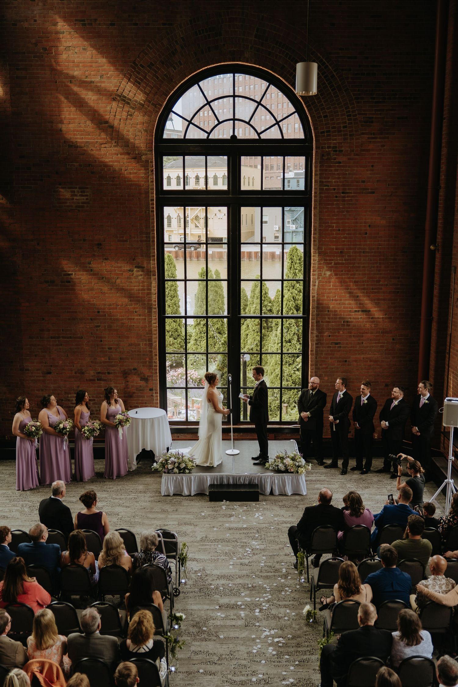 Wedding ceremony in an elegant brick venue with large arched windows.