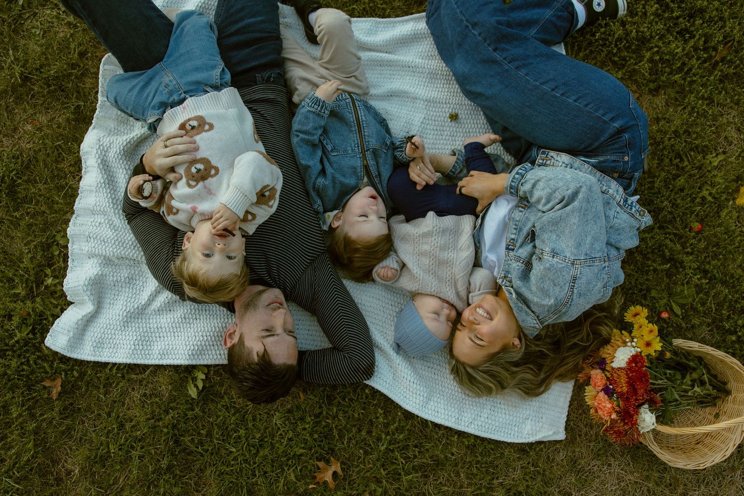 Overhead view of people lying on a white blanket on grass with a picnic basket nearby.