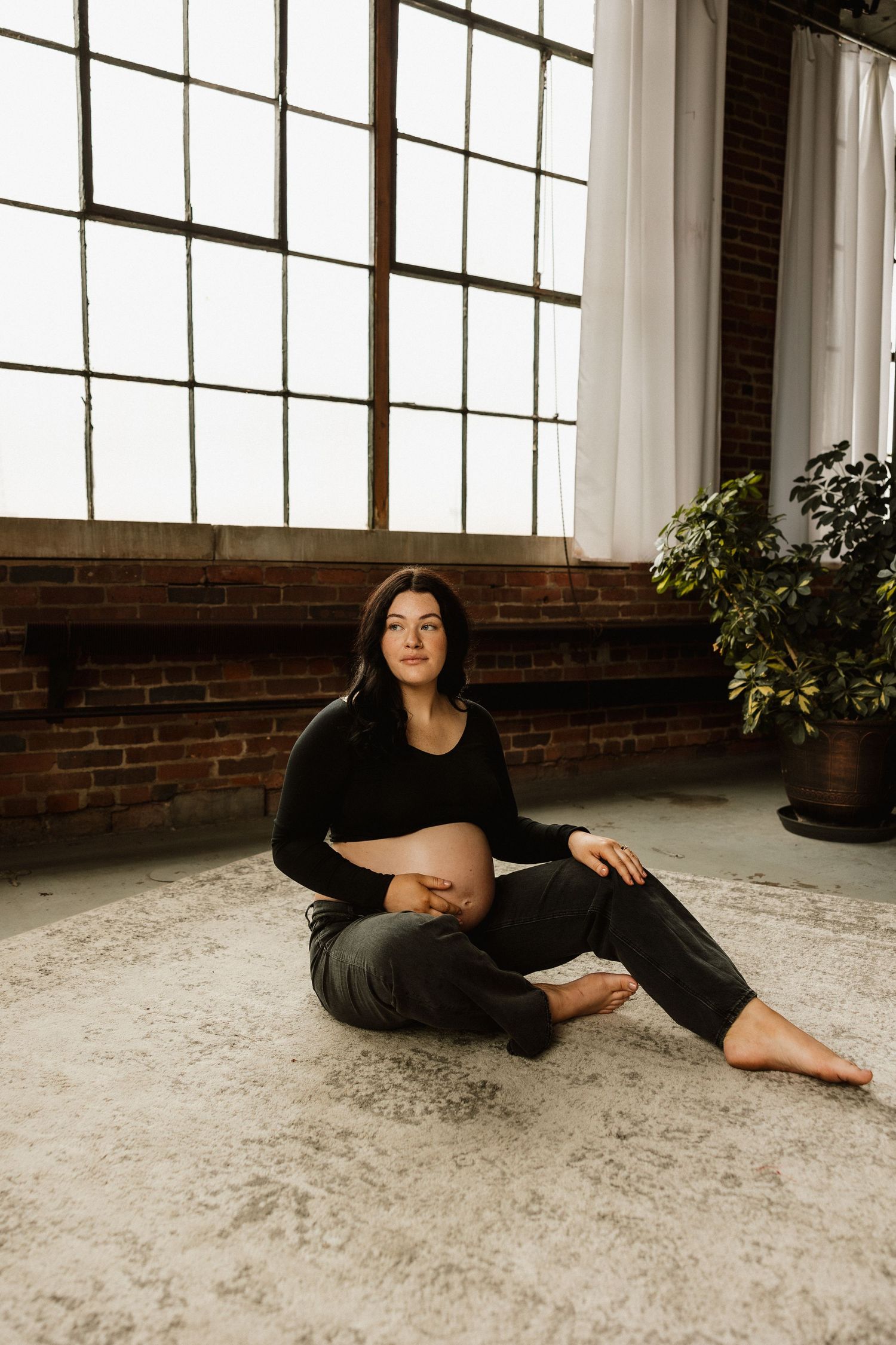 Artistic portrait series showing a person in black attire reclining on a light carpet against industrial windows and brick.