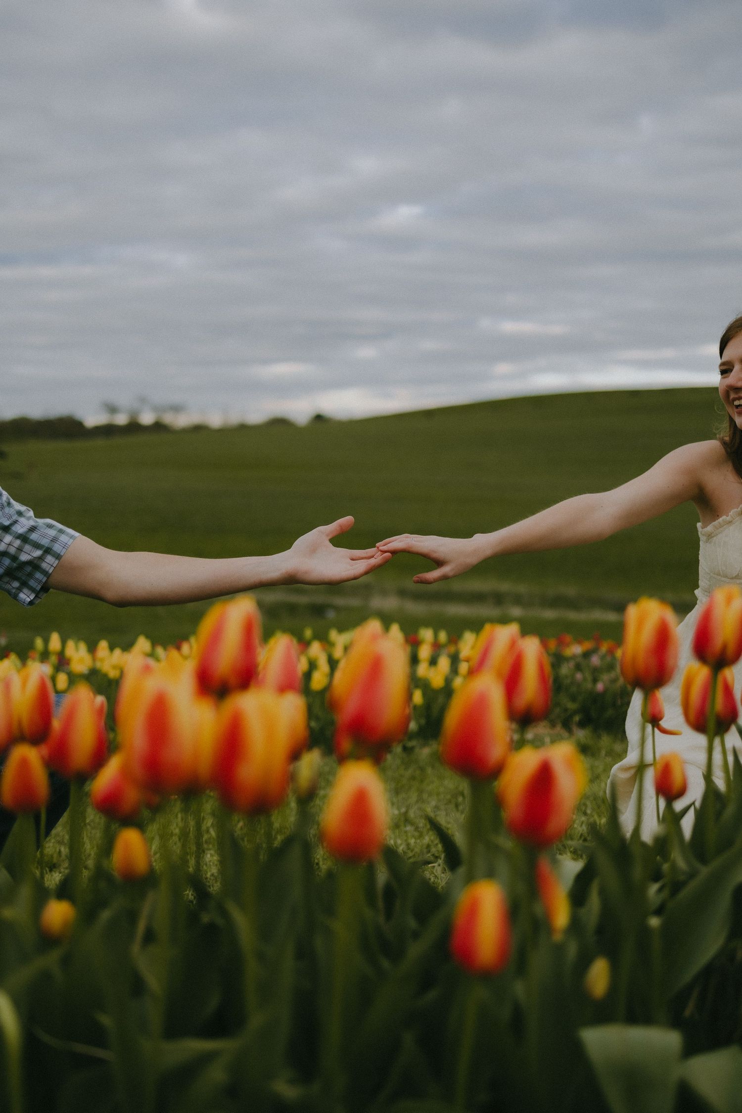 Two people reaching towards each other in a vibrant tulip garden.