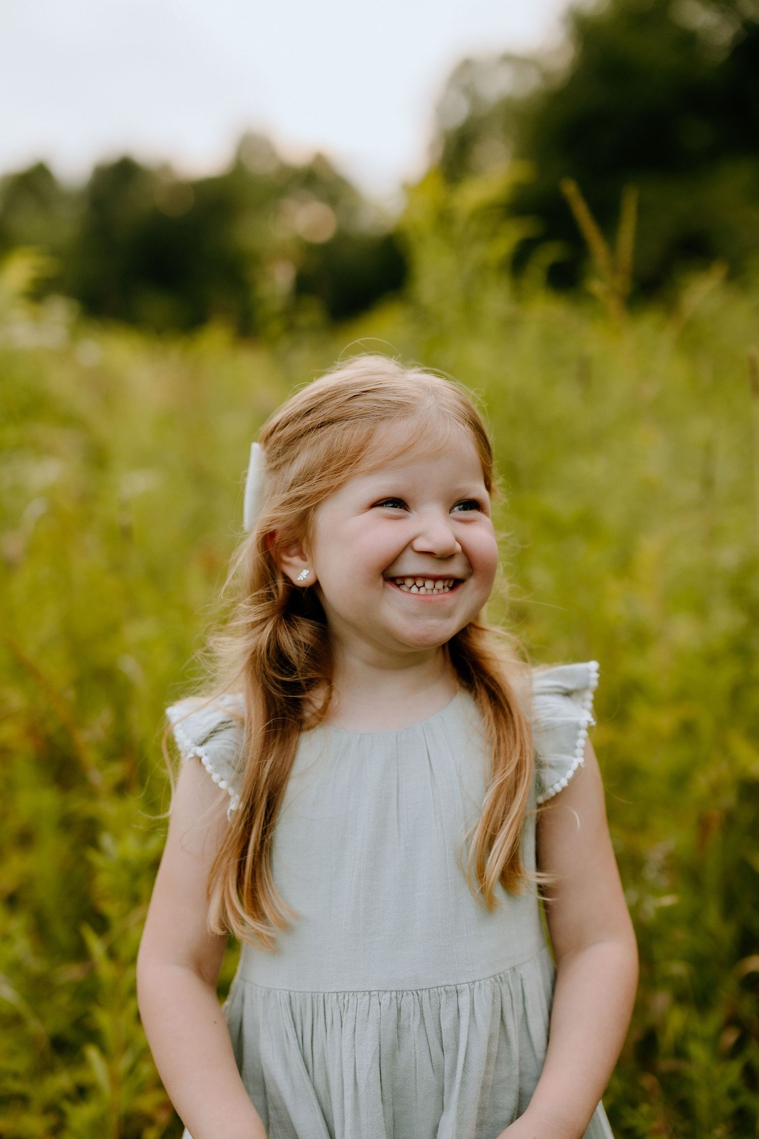 Young child in a light dress smiling brightly in a summer meadow.