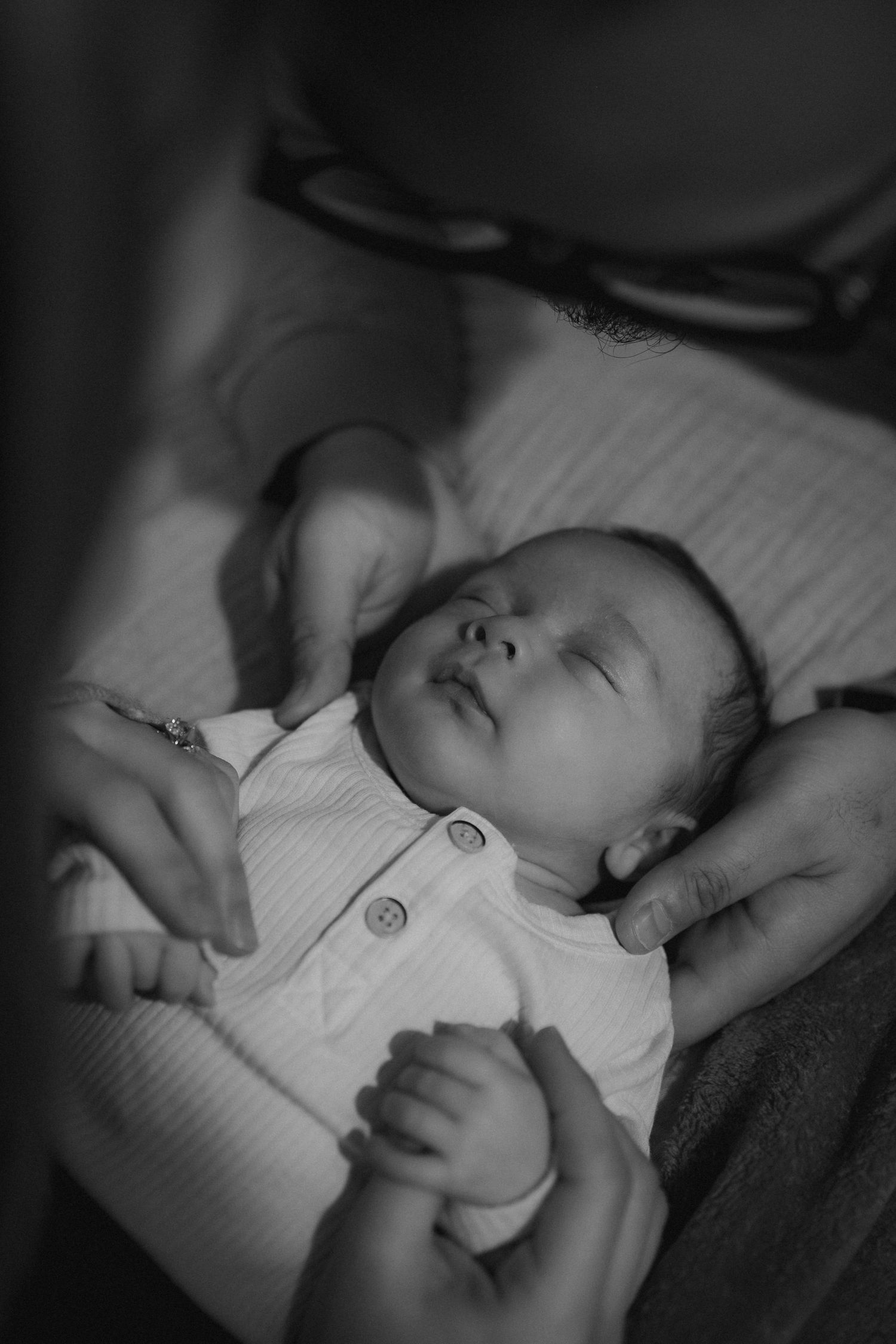 A peaceful black and white image of a sleeping baby in a white outfit.