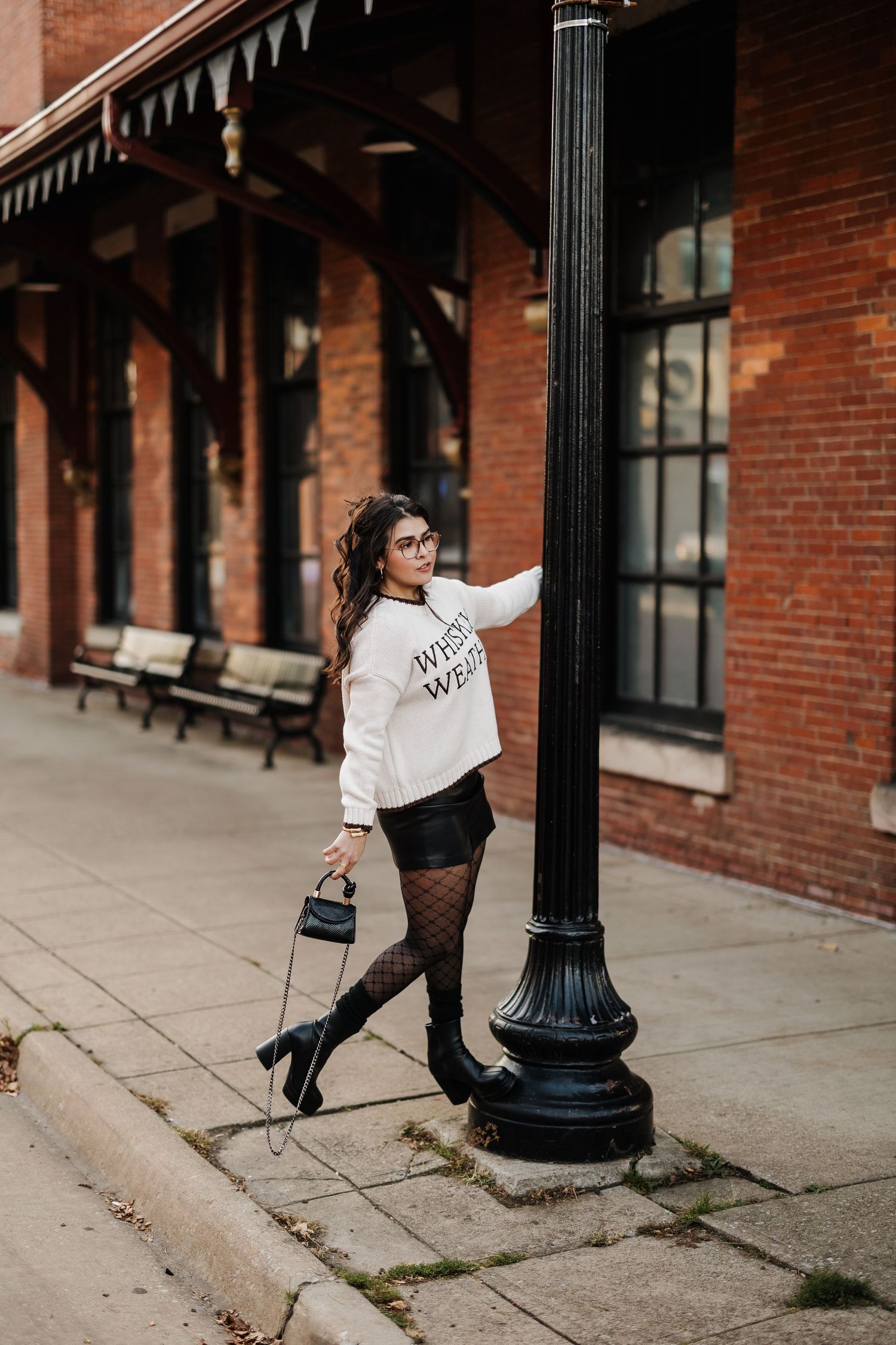Urban fashion photo against historic brick building with white sweater and black accessories.