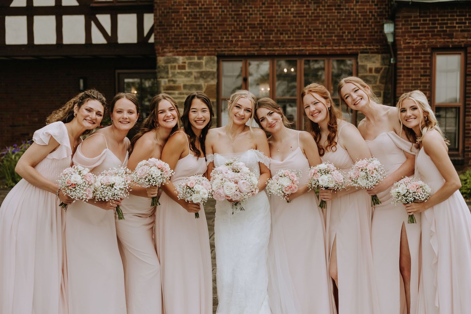A row of bridesmaids in pink dresses standing together and smiling while holding matching floral bouquets.