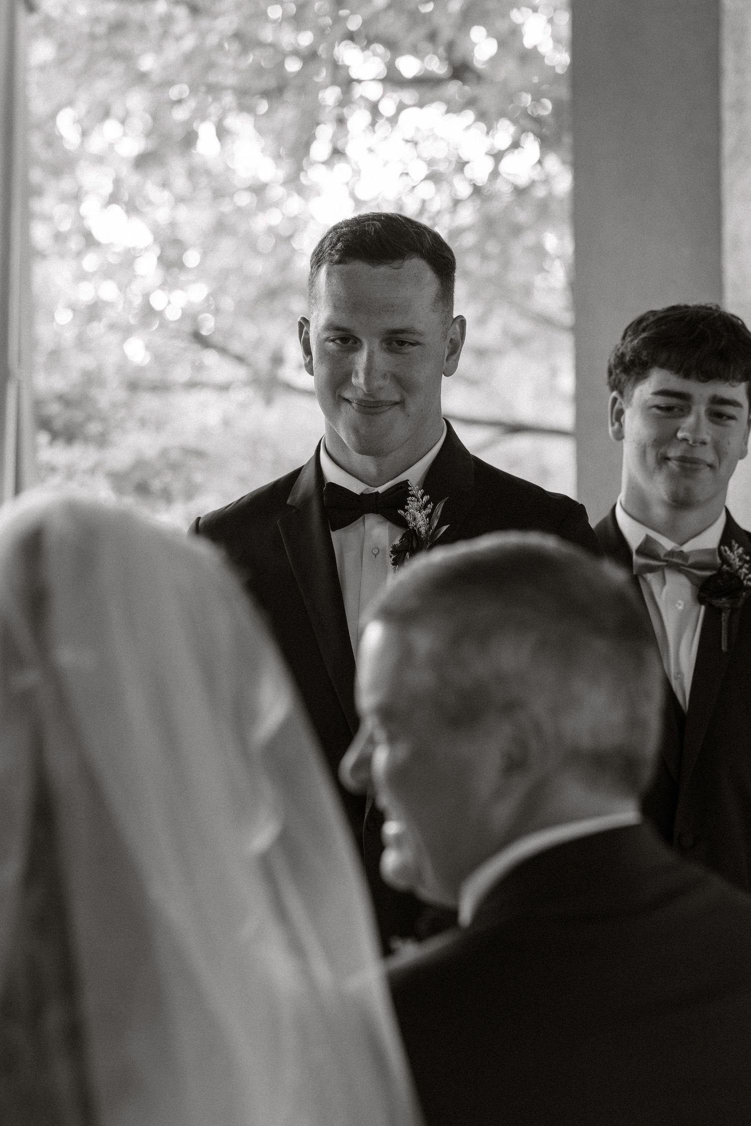 Black and white photo of formal wedding ceremony with attendees in tuxedos and bow ties.