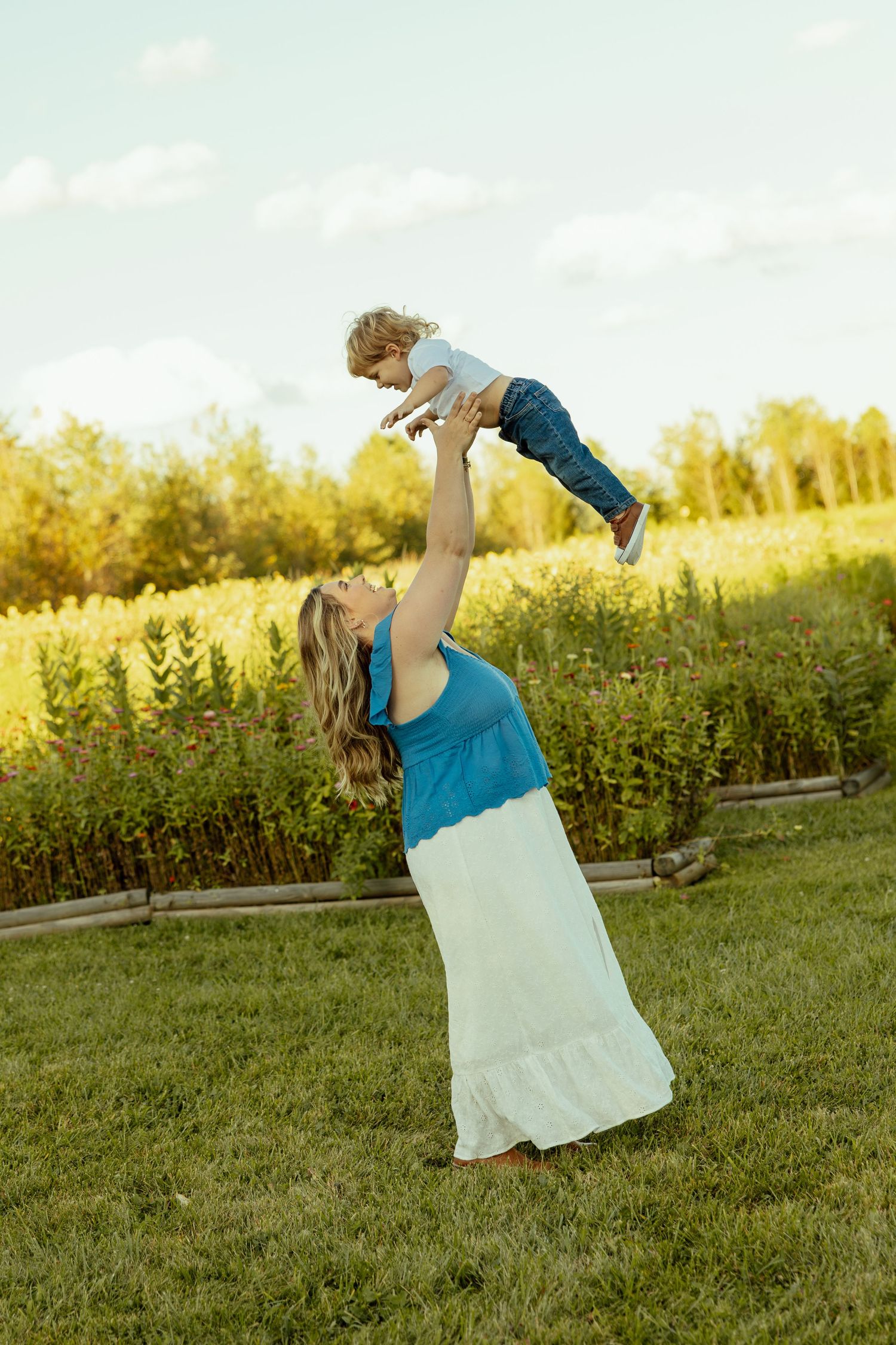 A person in a blue top and white skirt performs a graceful dance movement in a sunlit meadow at golden hour.