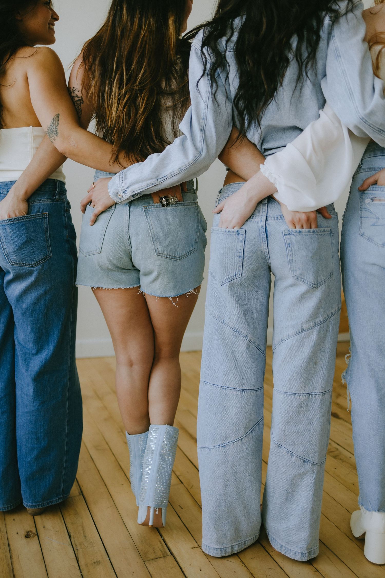 Three people wearing denim stand in a row showing off their jeans on a wooden deck.