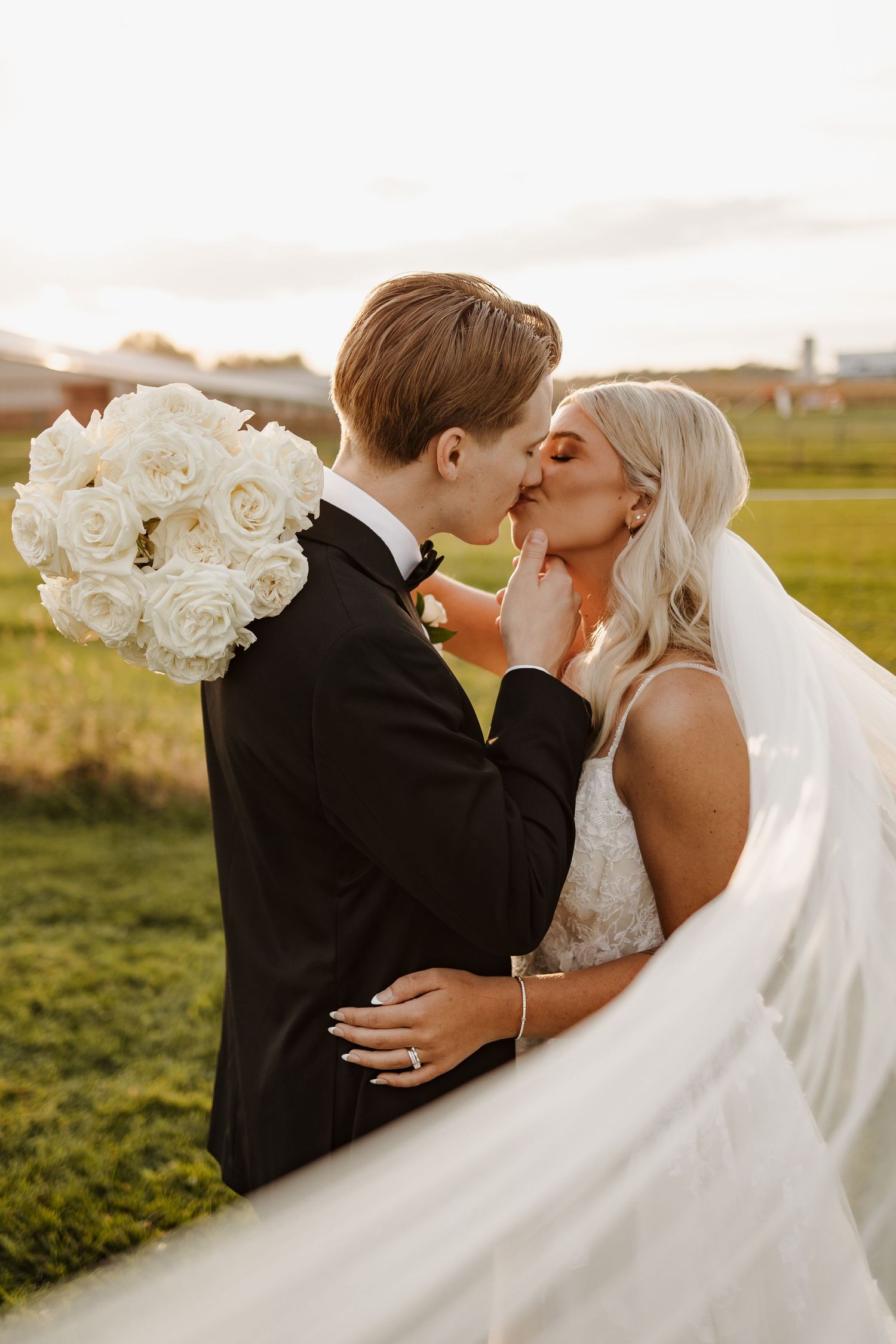 Romantic sunset wedding portrait with white rose bouquet and flowing veil.