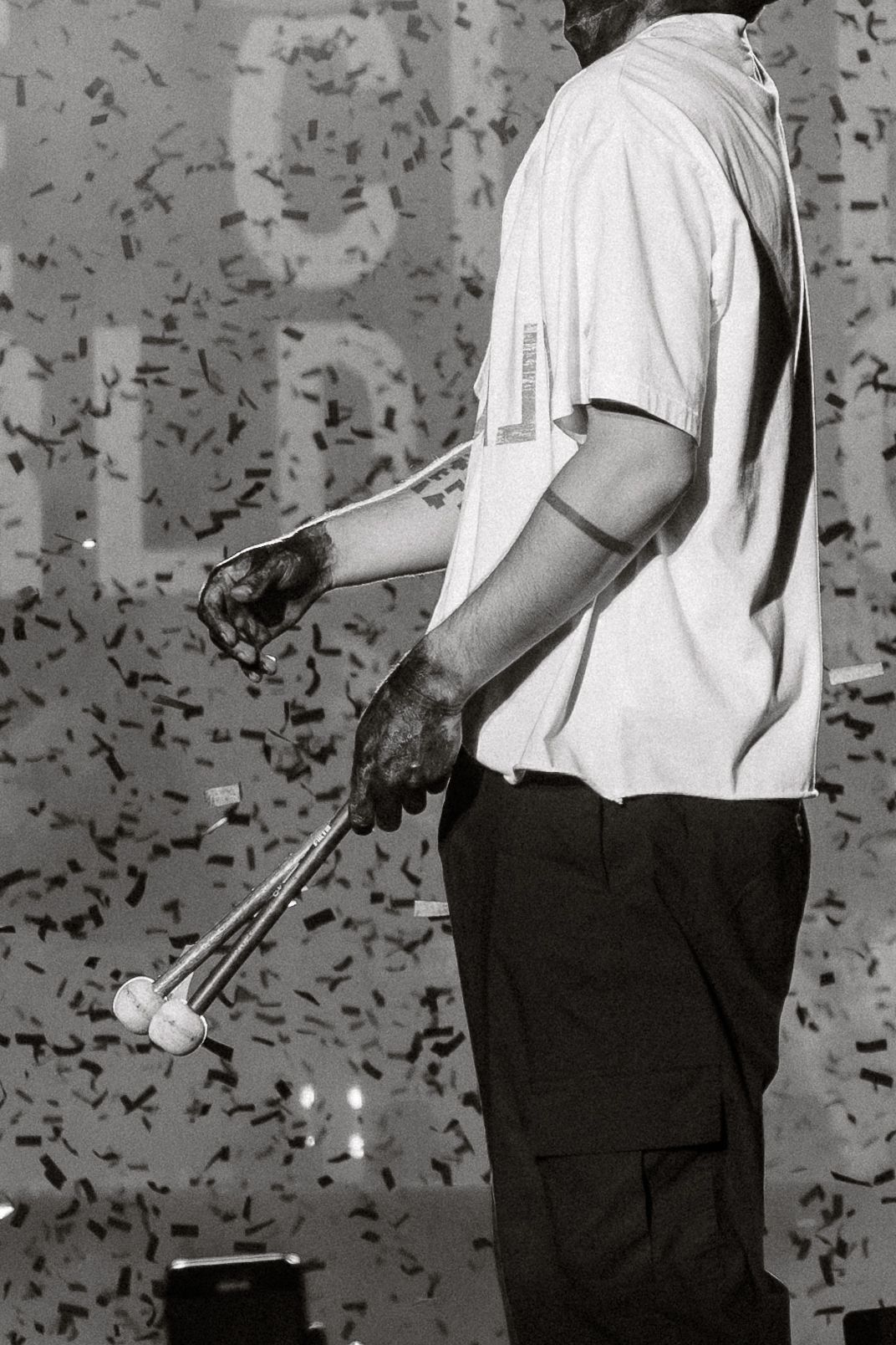 Black and white photo of performer holding drumsticks against textured background with confetti.
