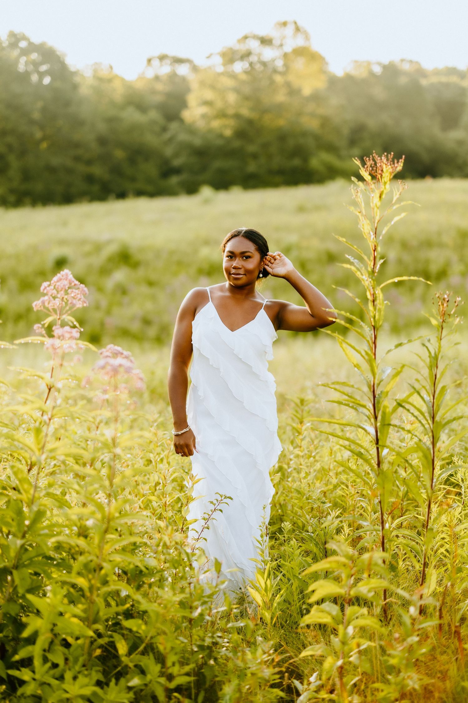 Figure in white dress standing among tall wildflowers at sunset.