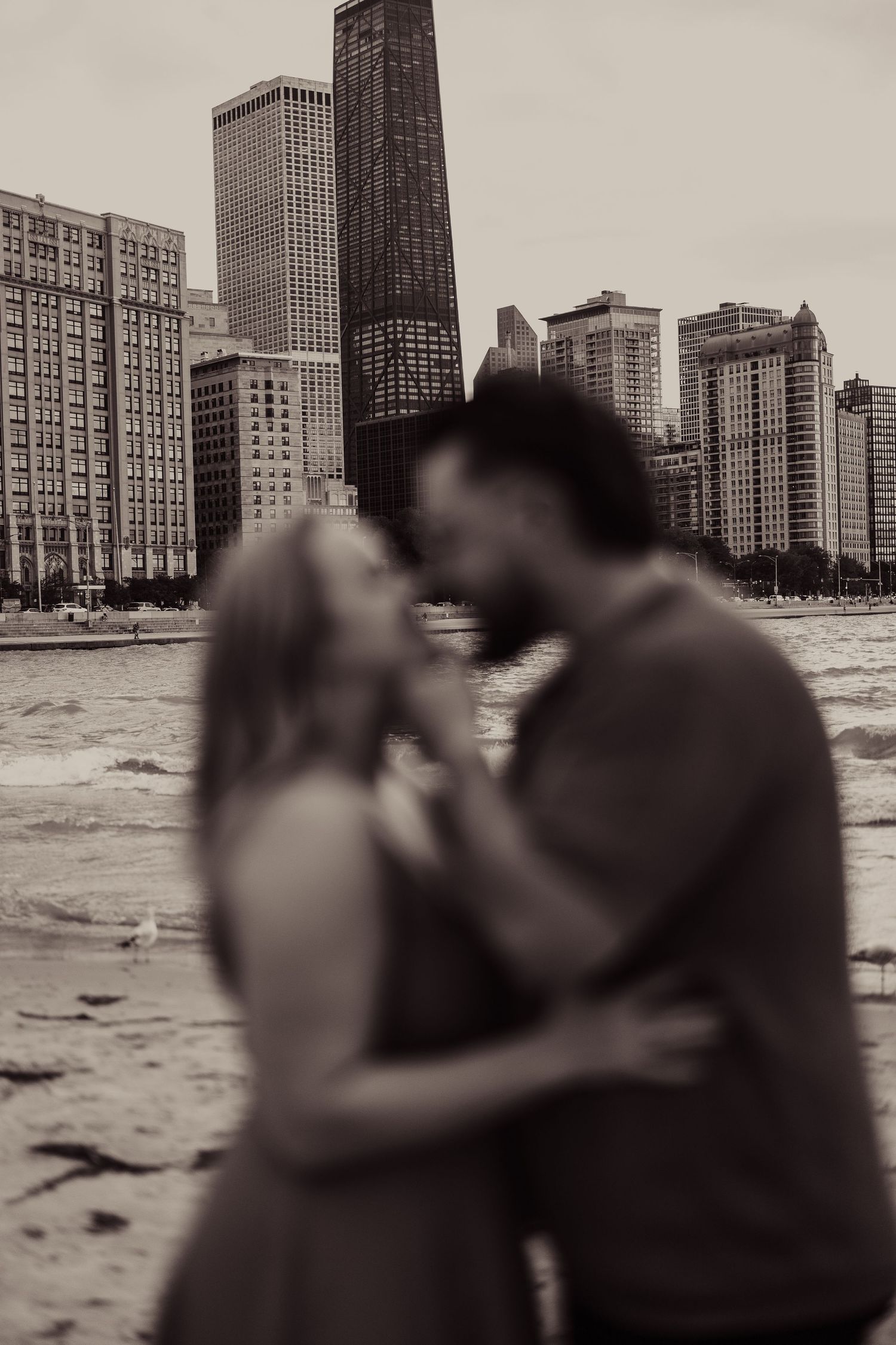A silhouetted couple embracing on the beach with Chicago's dramatic architectural skyline behind them.