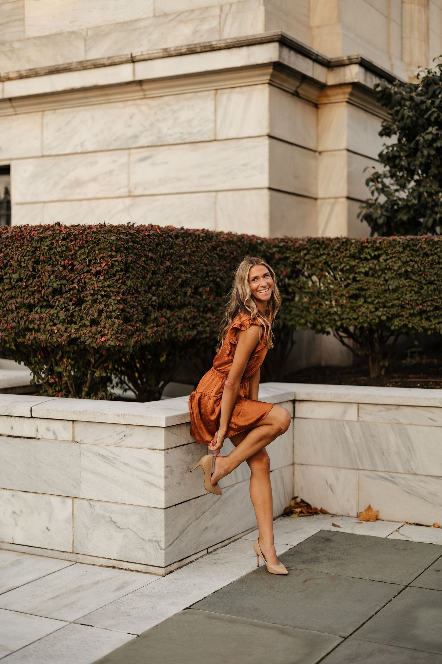 A fashion portrait shows someone in an autumn dress sitting on marble steps near ivy-covered walls.