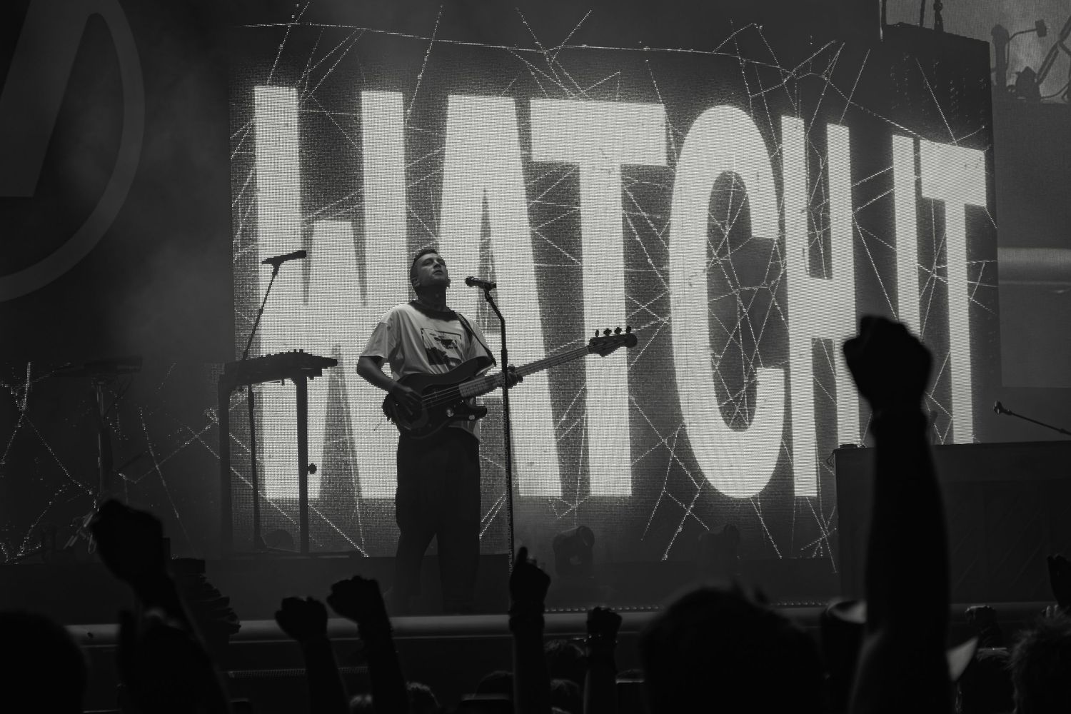 Musician performs on stage with large HATCHET text projected behind them in black and white.