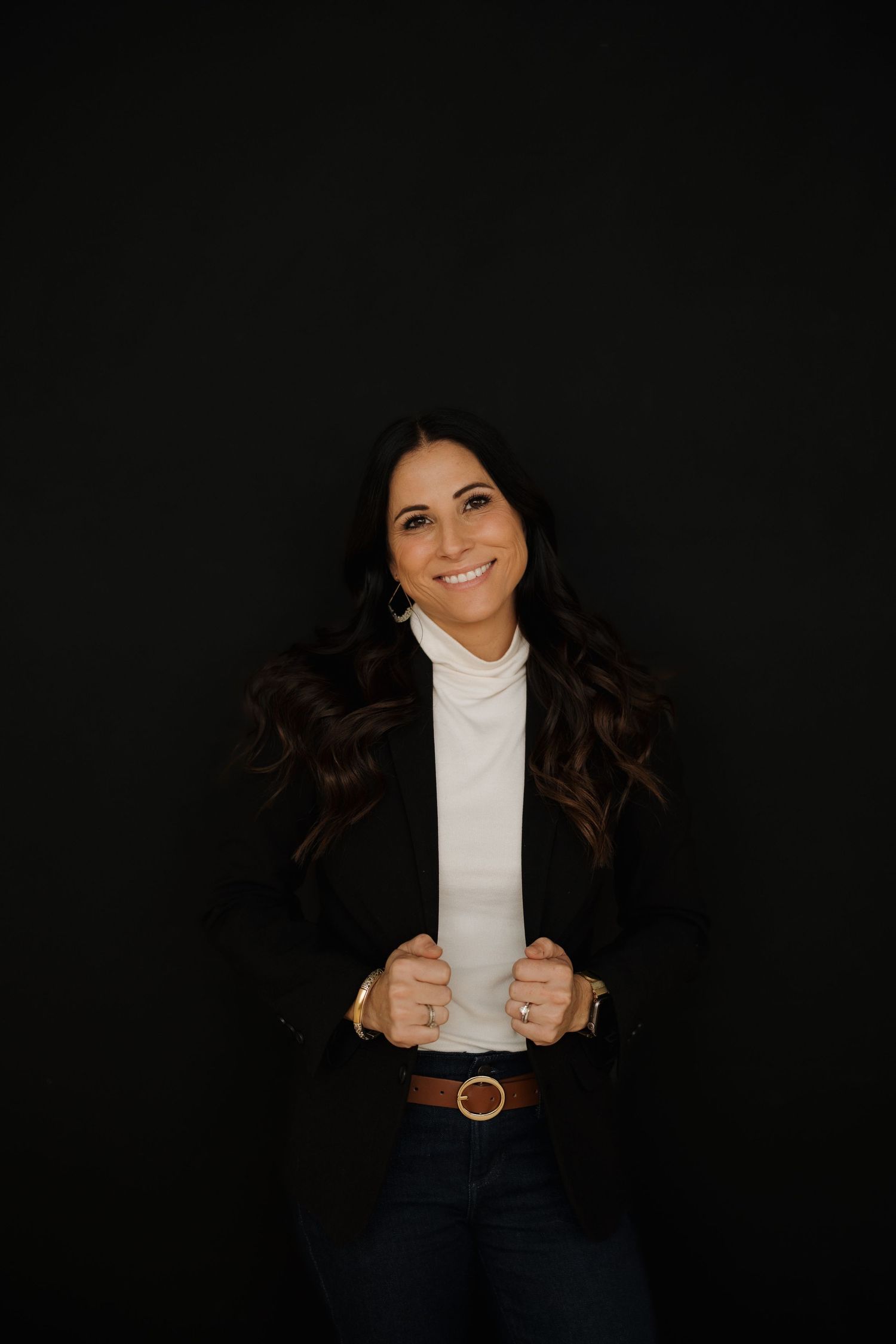 Portrait in business attire with turtleneck and blazer against dark background.