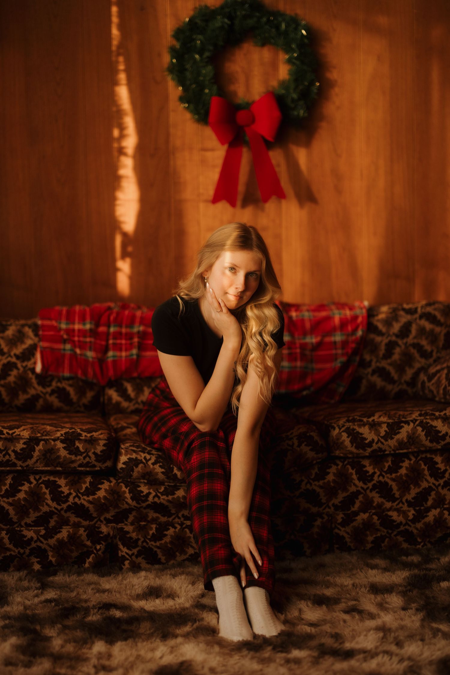 Cozy holiday scene with Christmas wreath, plaid pillows, and person on brown couch.