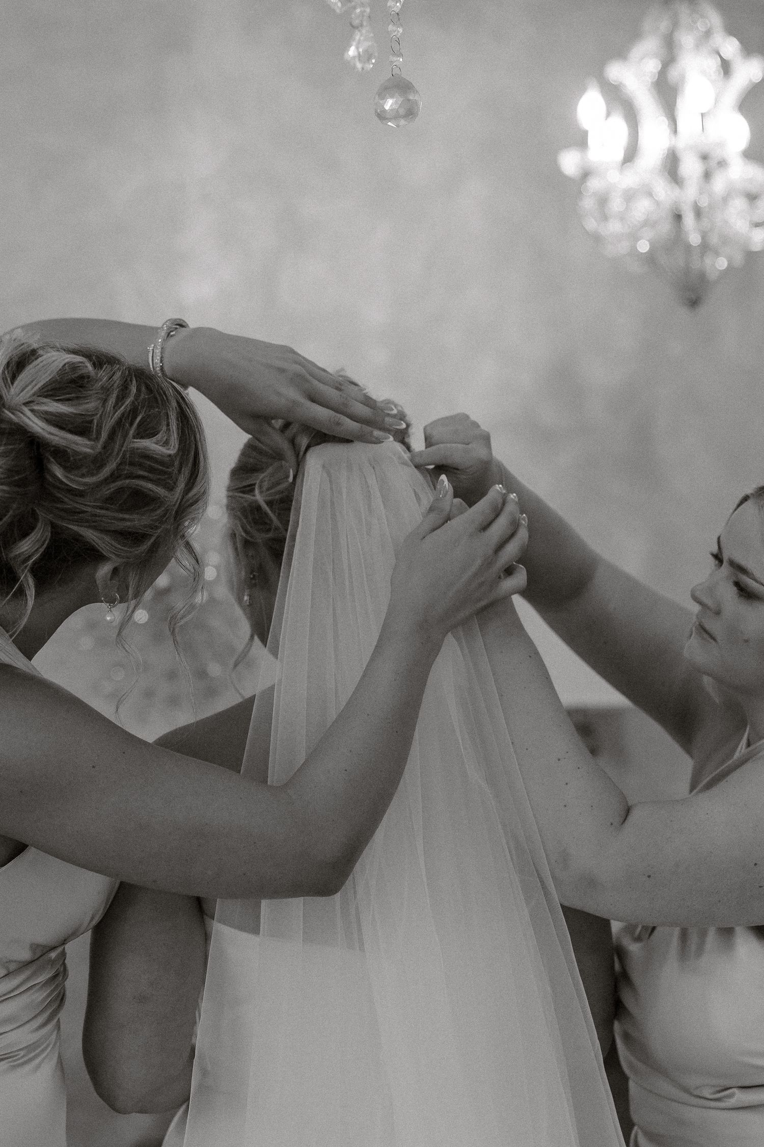 A series of black and white photos showing hands adjusting a delicate bridal veil under elegant crystal chandeliers.