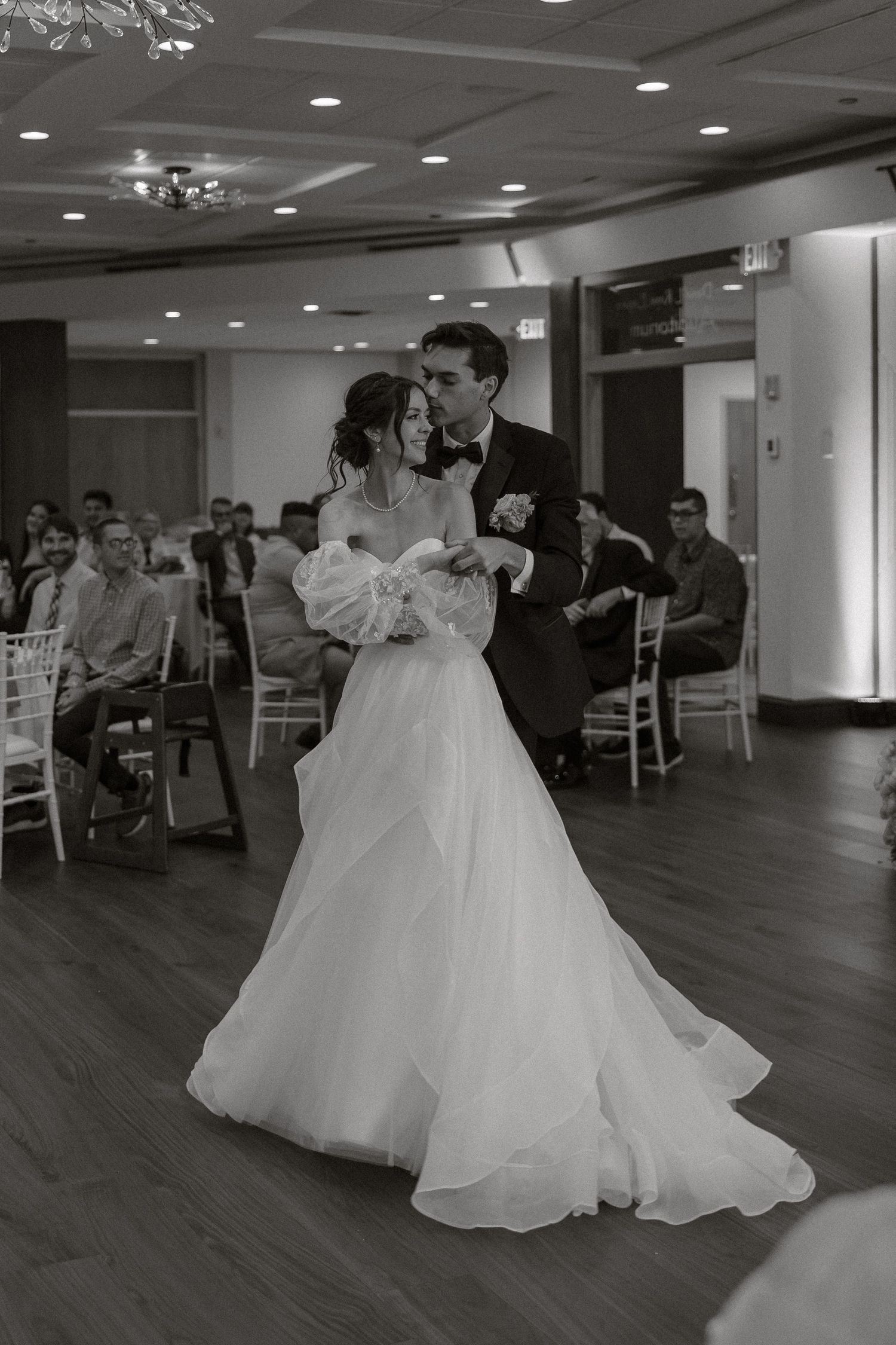 A couple dances in an elegant indoor reception venue with white decor and hardwood floors.