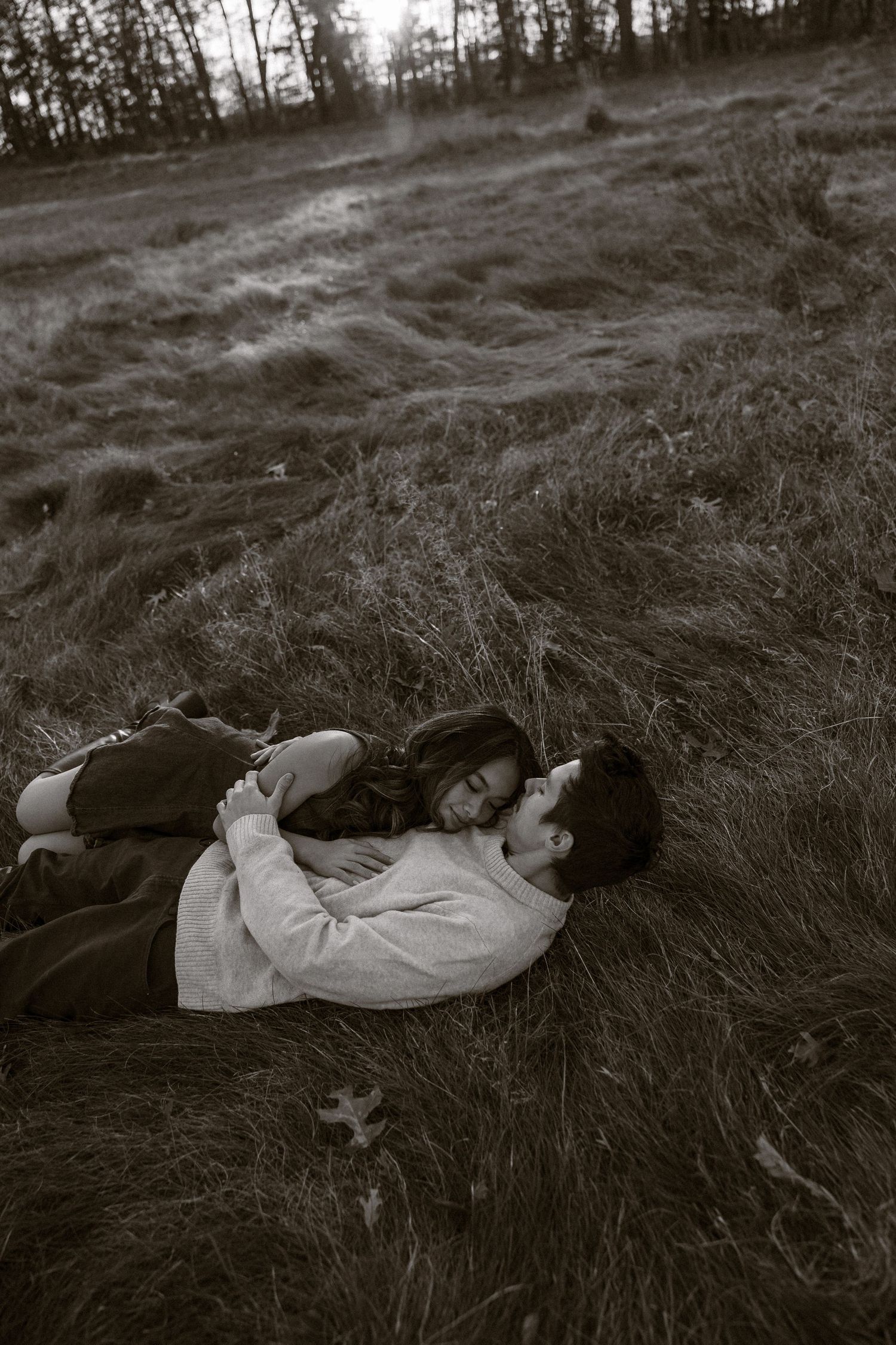 A romantic black and white photo series showing a couple lying in tall grass at sunset.