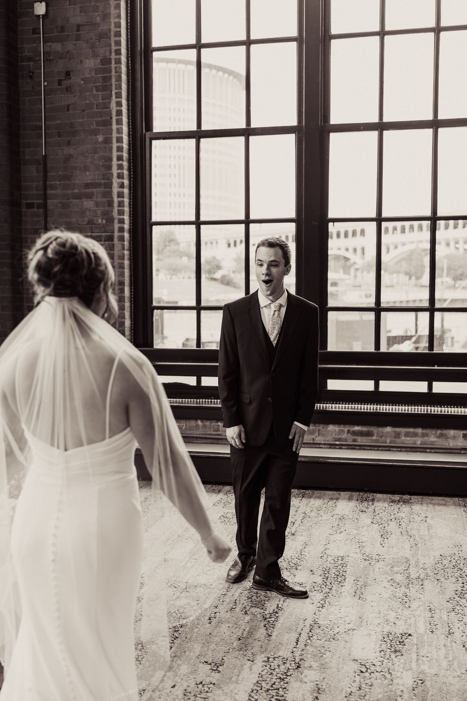 Wedding couple silhouetted against large industrial windows in an urban loft space.