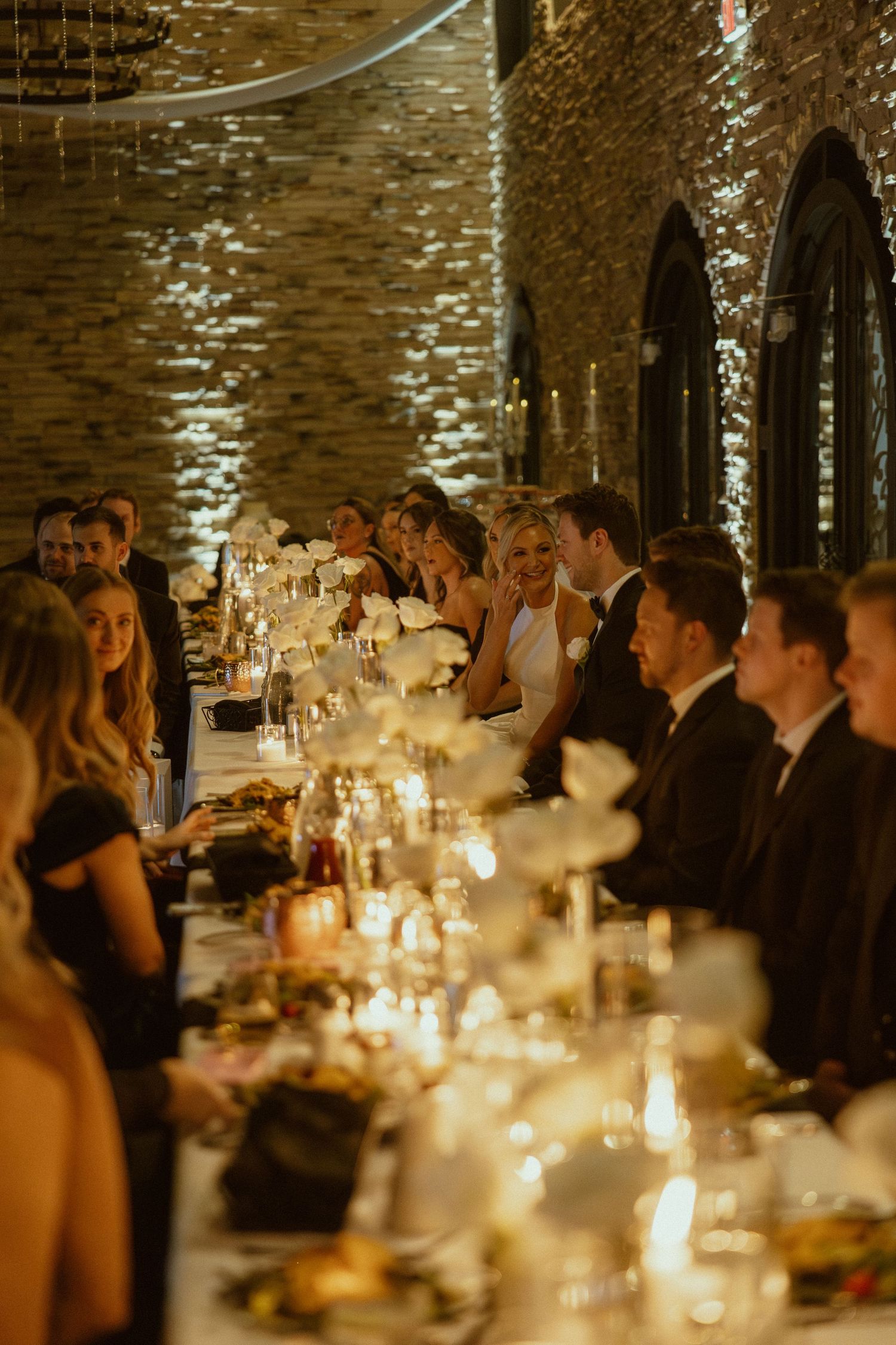 Wedding reception dinner in a rustic venue with warm candlelight illuminating the long tables.
