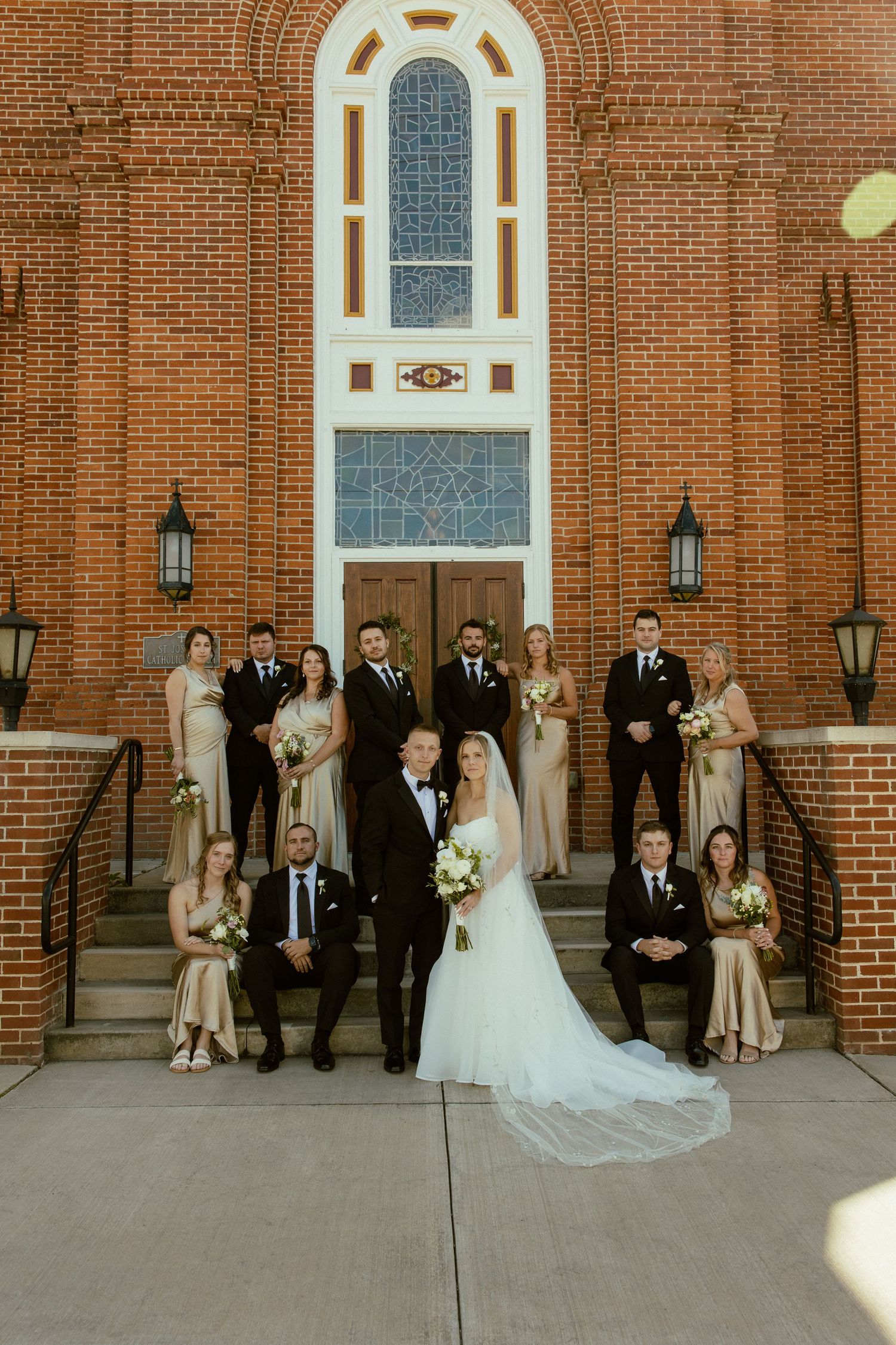 Wedding party poses for formal photos outside a classic red brick church.