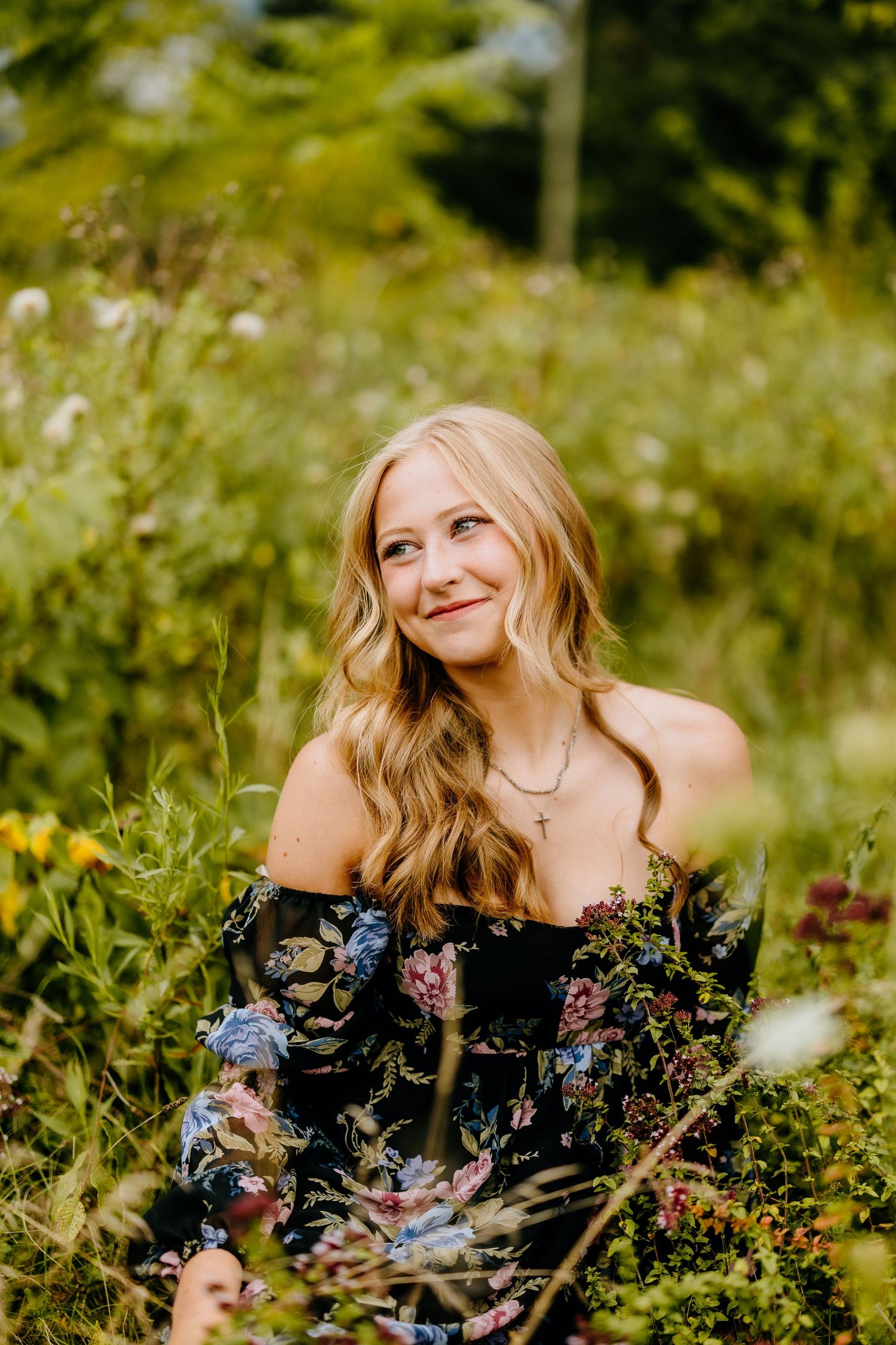 Person in off-shoulder floral dress poses amidst wildflowers in summer meadow.