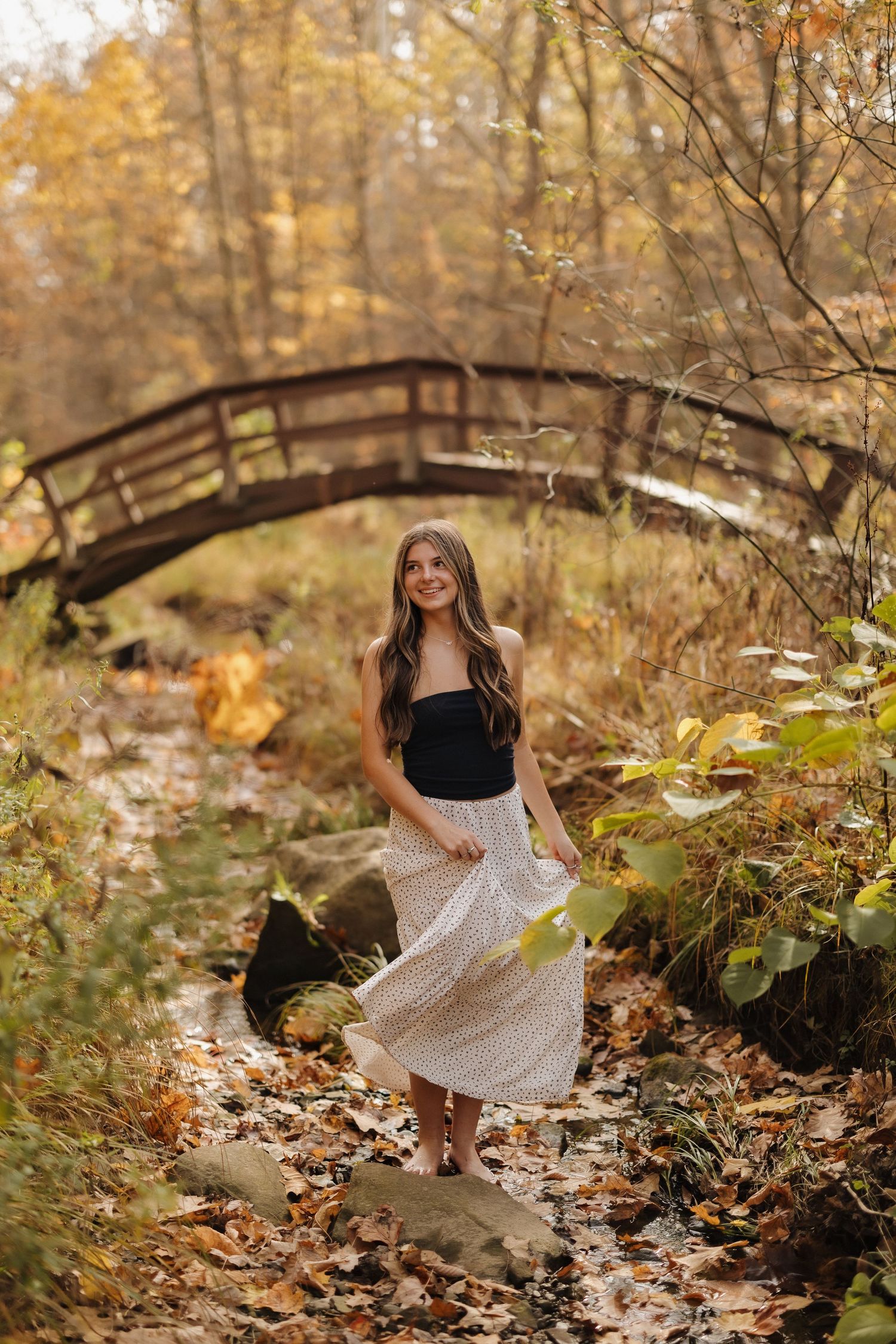 A flowing white skirt twirls against an autumn backdrop with a rustic wooden bridge.