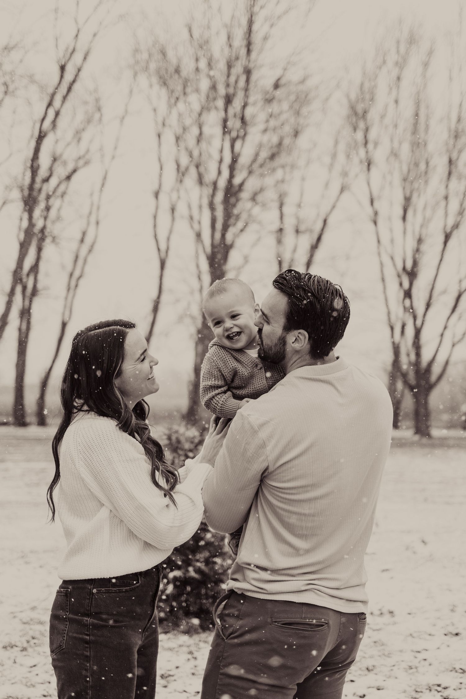 Family shares intimate moment in snowy setting with bare trees.