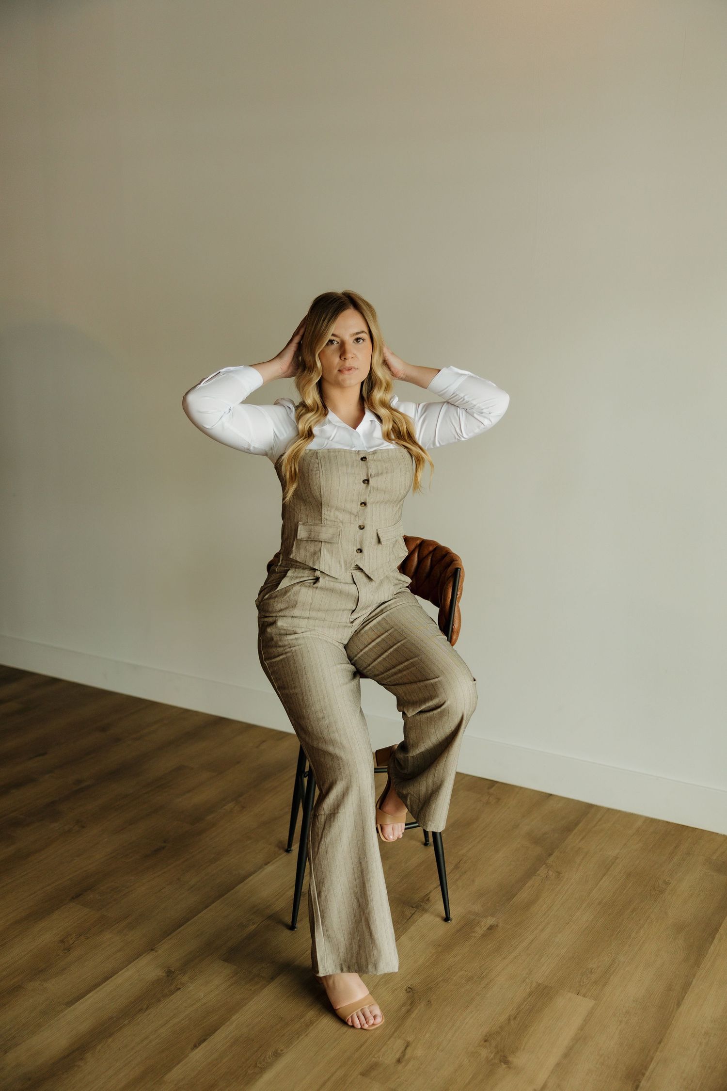 Casual business portrait in beige jumpsuit and white blouse sitting on wooden chair.