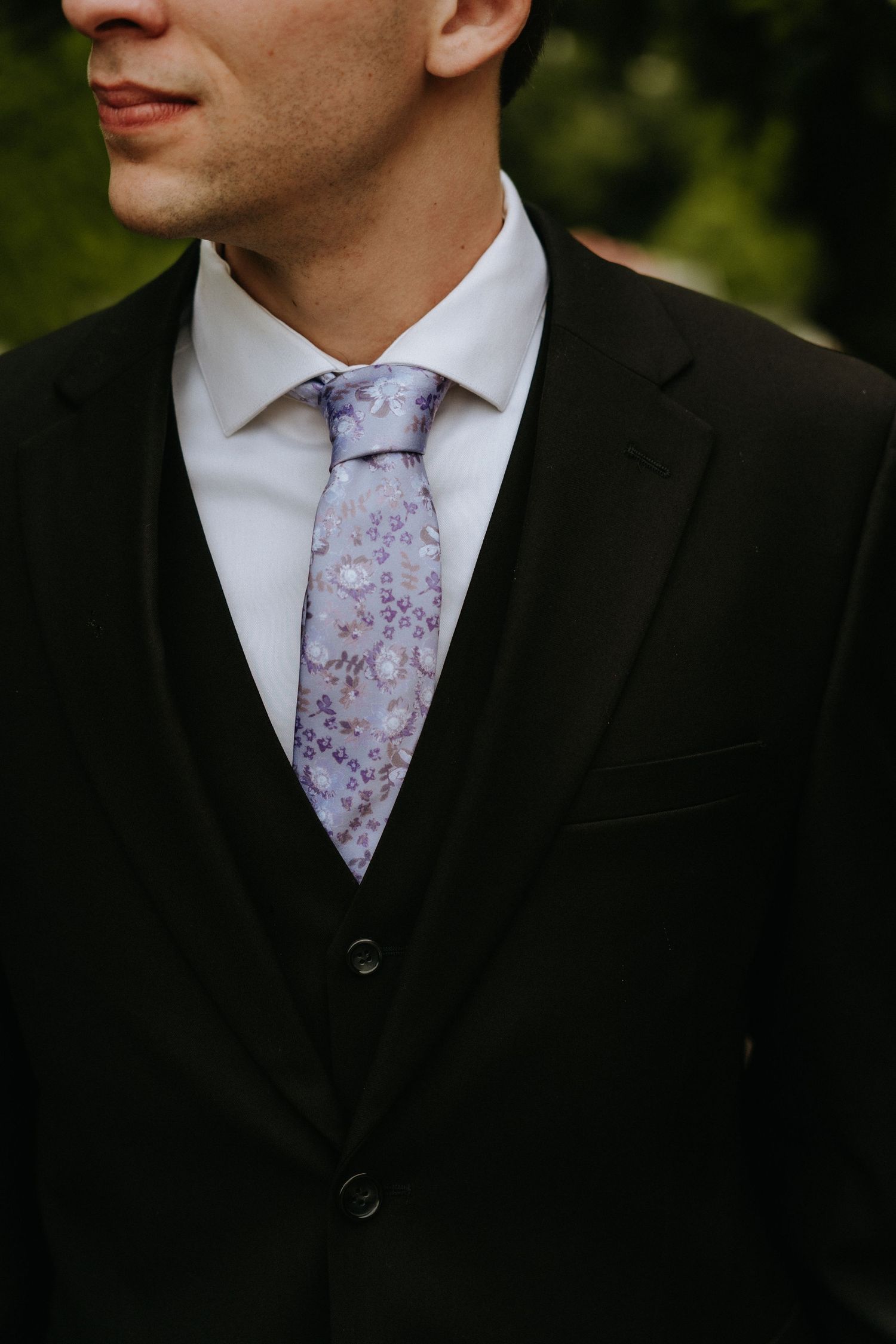 Close-up detail of a black suit jacket with a light purple floral patterned tie.