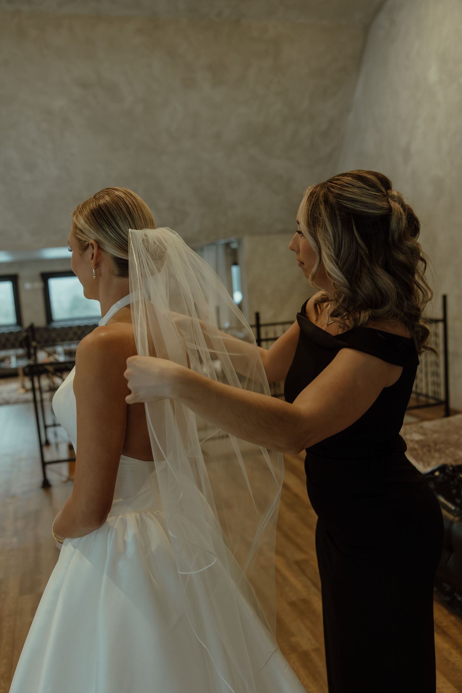 A wedding veil being adjusted and arranged by someone wearing a black dress.