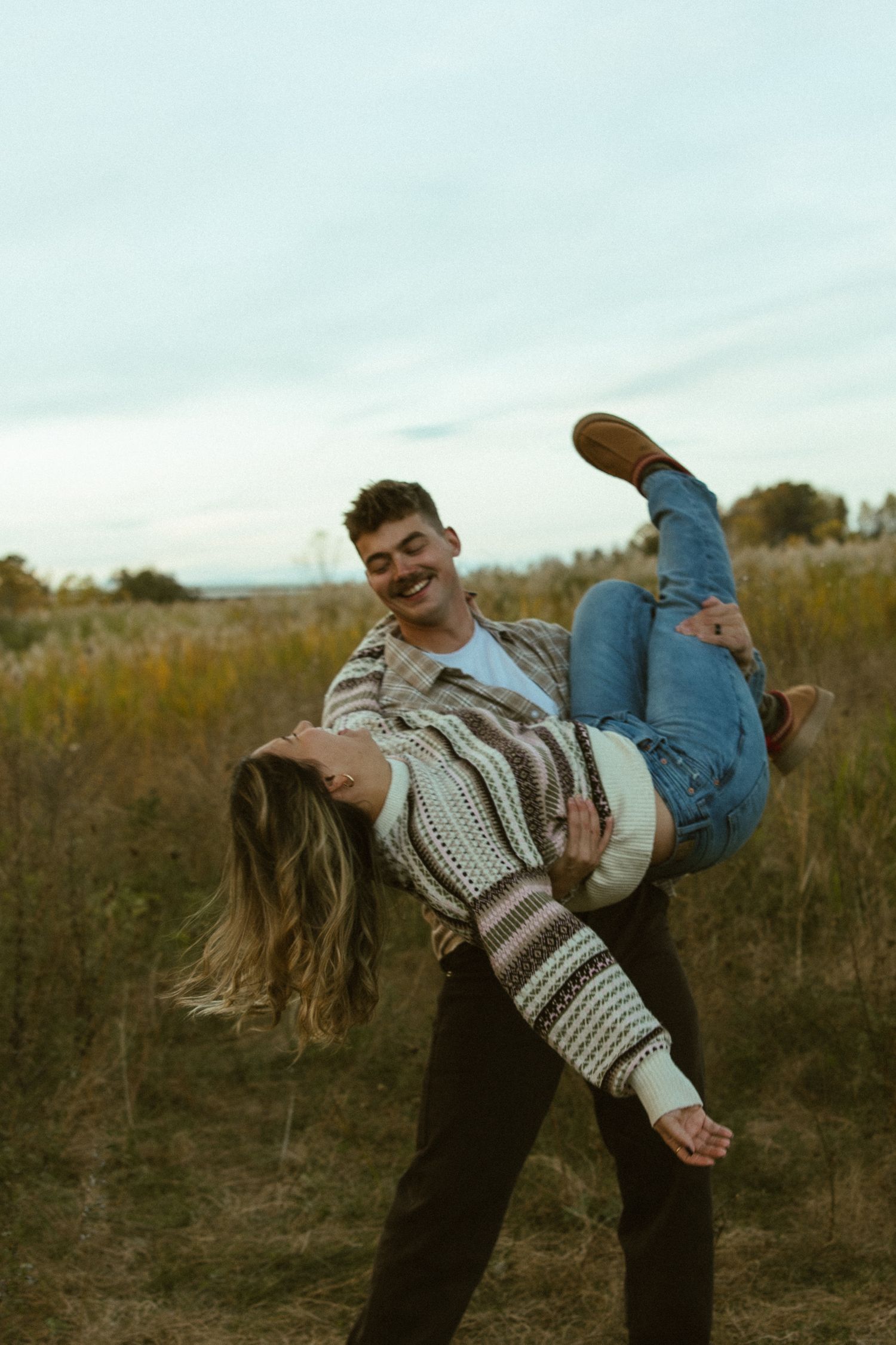 A playful couple dances in a field during golden hour, creating a romantic and carefree moment.