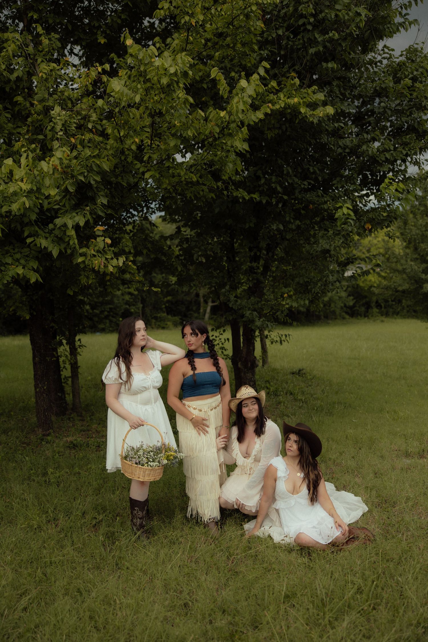 A group in white and cream dresses sits together on grassy field during golden hour in a natural outdoor setting.