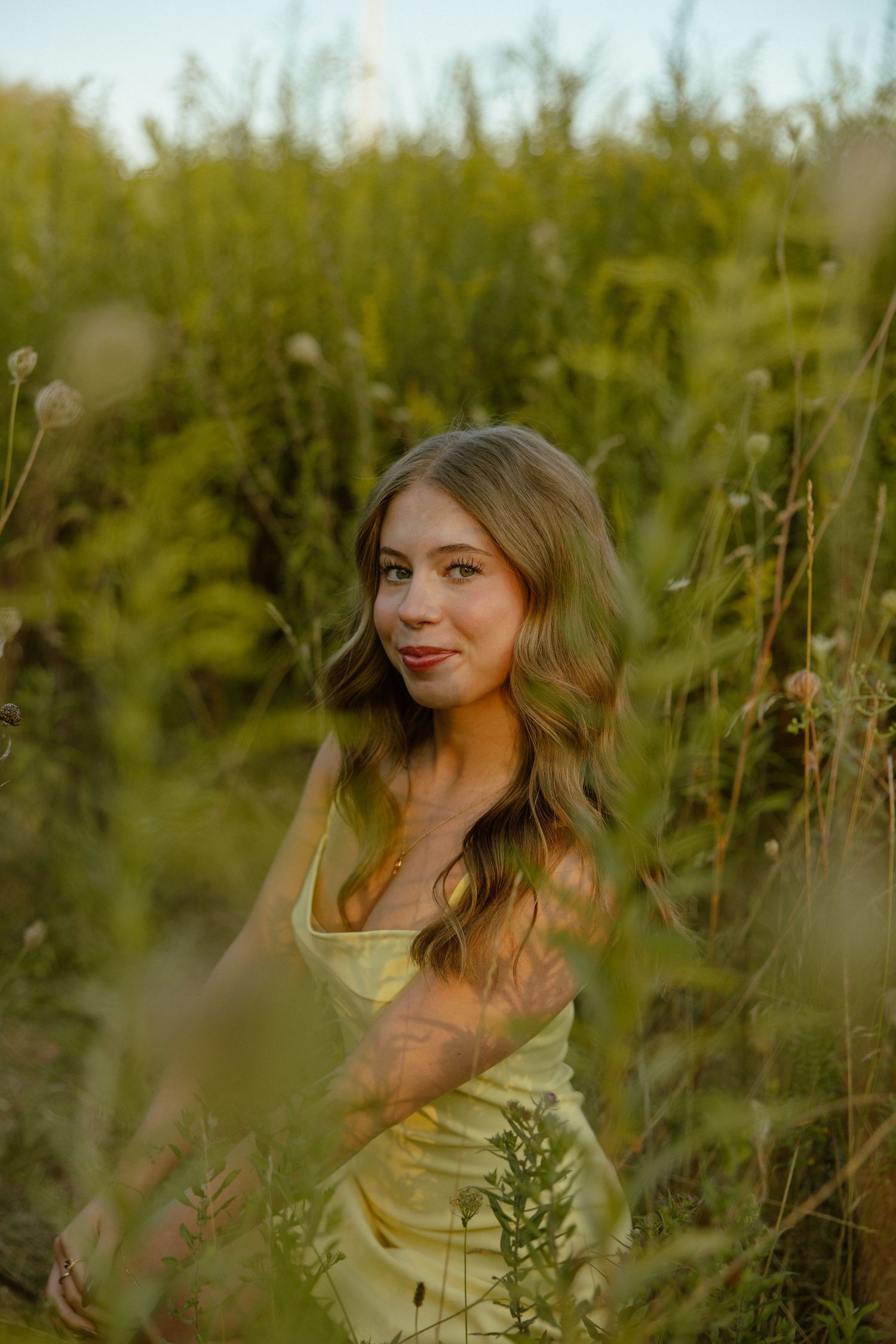 Portrait session in tall grass with soft natural lighting and green foliage creating a romantic atmosphere.