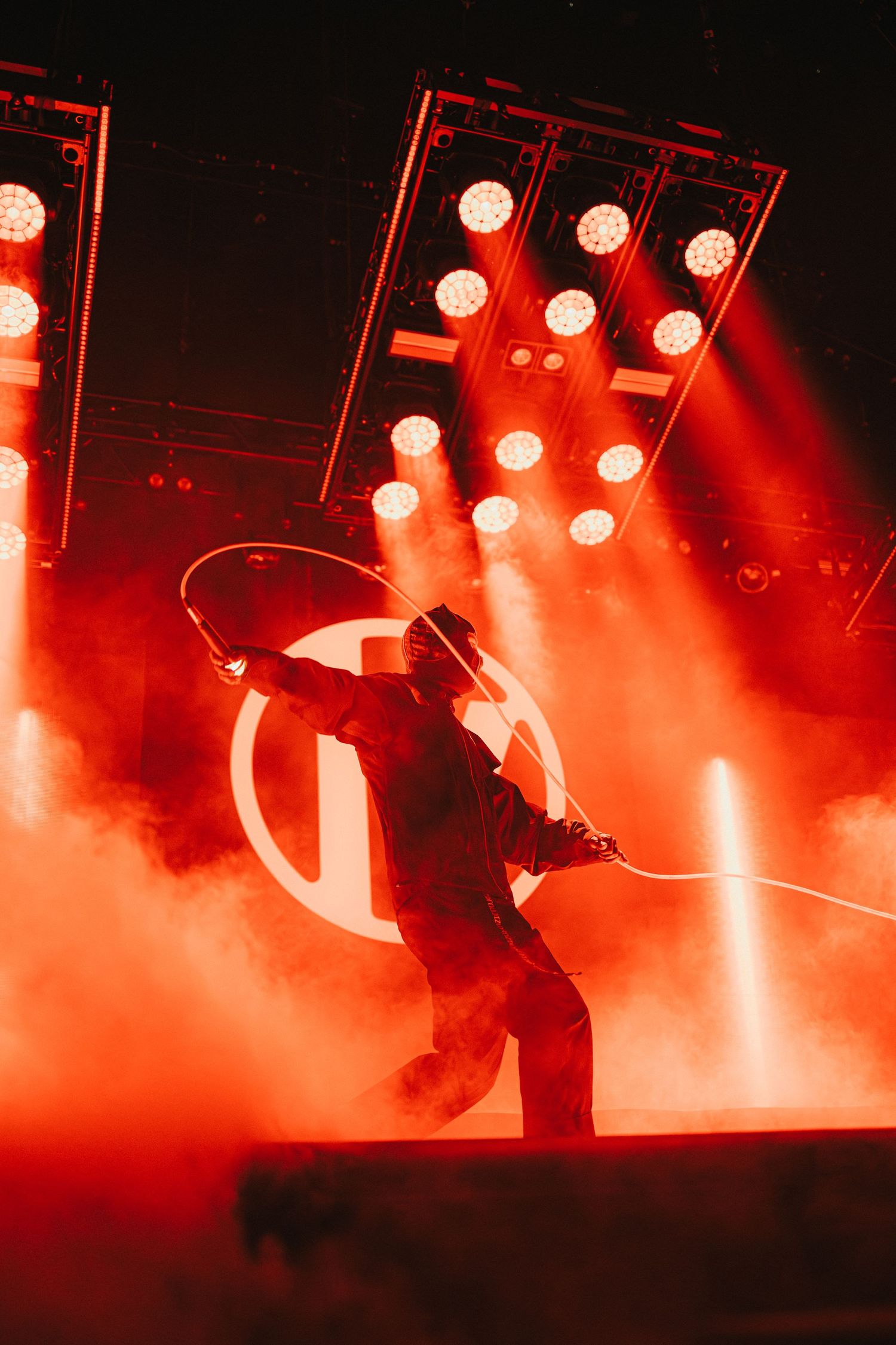 Performer silhouetted against bright red stage lights and fog during dynamic concert performance.
