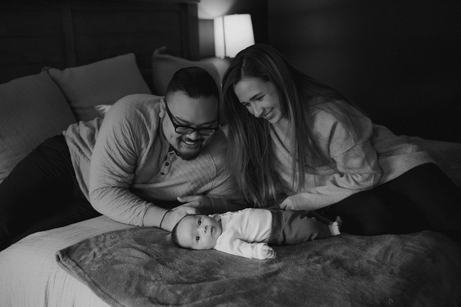 Intimate black and white image of parents admiring their newborn on a bed.