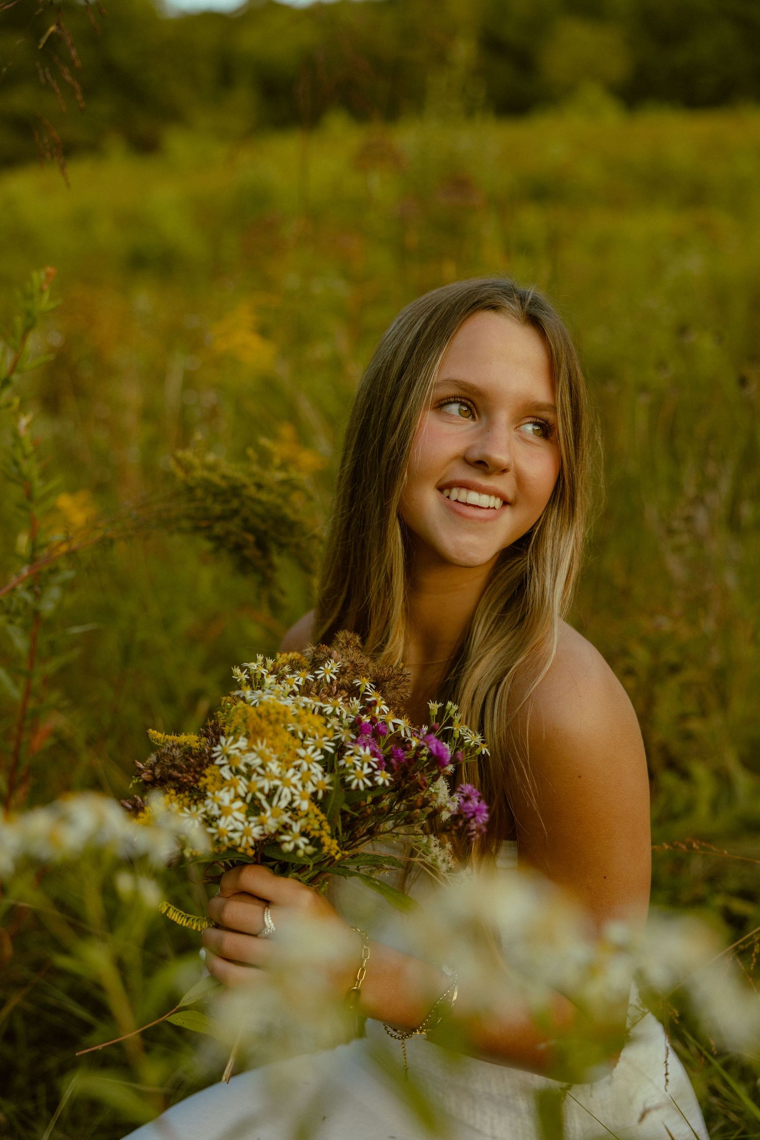 A person poses joyfully in a golden meadow at sunset holding freshly picked wildflowers in their hands.