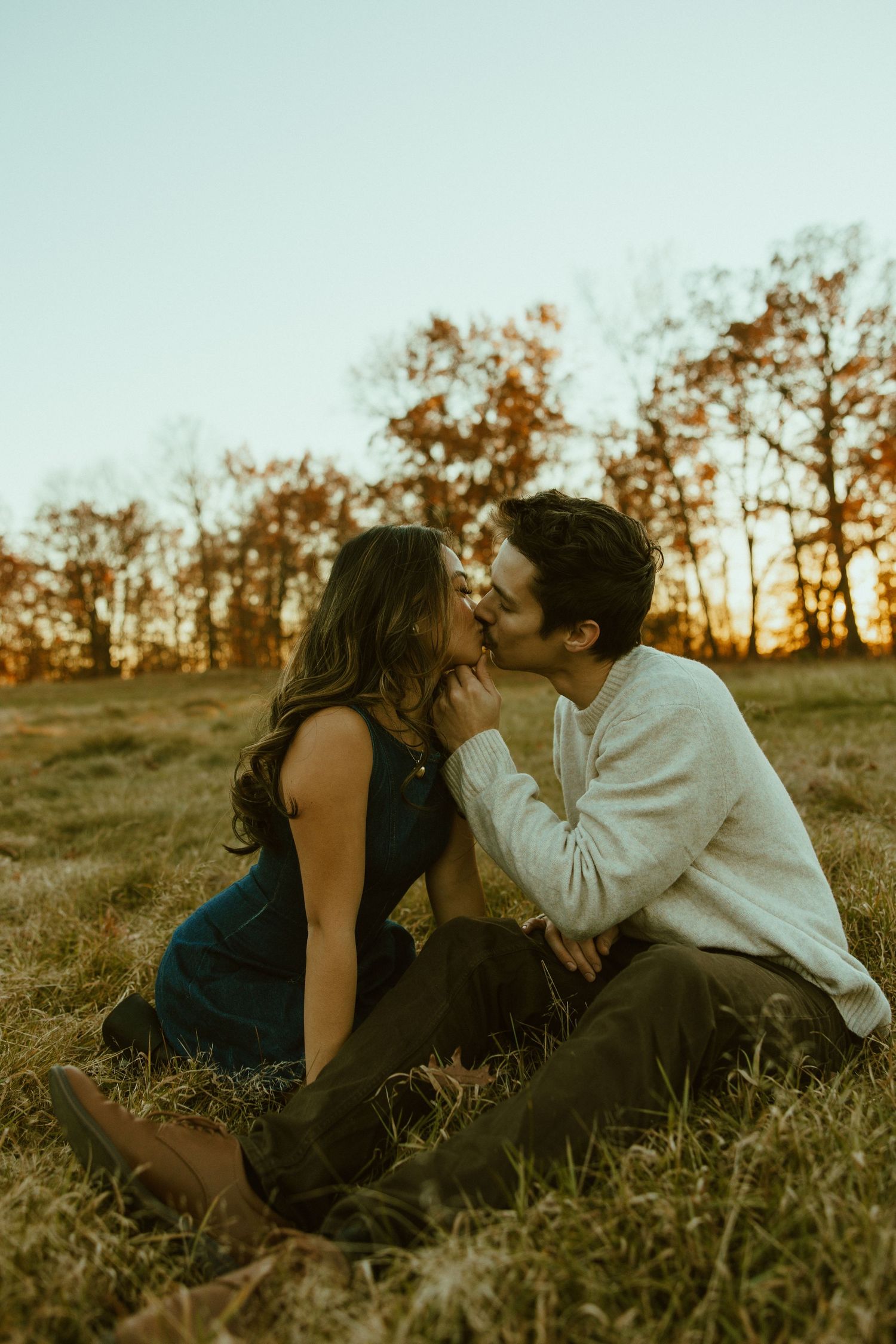 A couple shares an intimate moment while sitting in a grassy field during golden hour sunset.