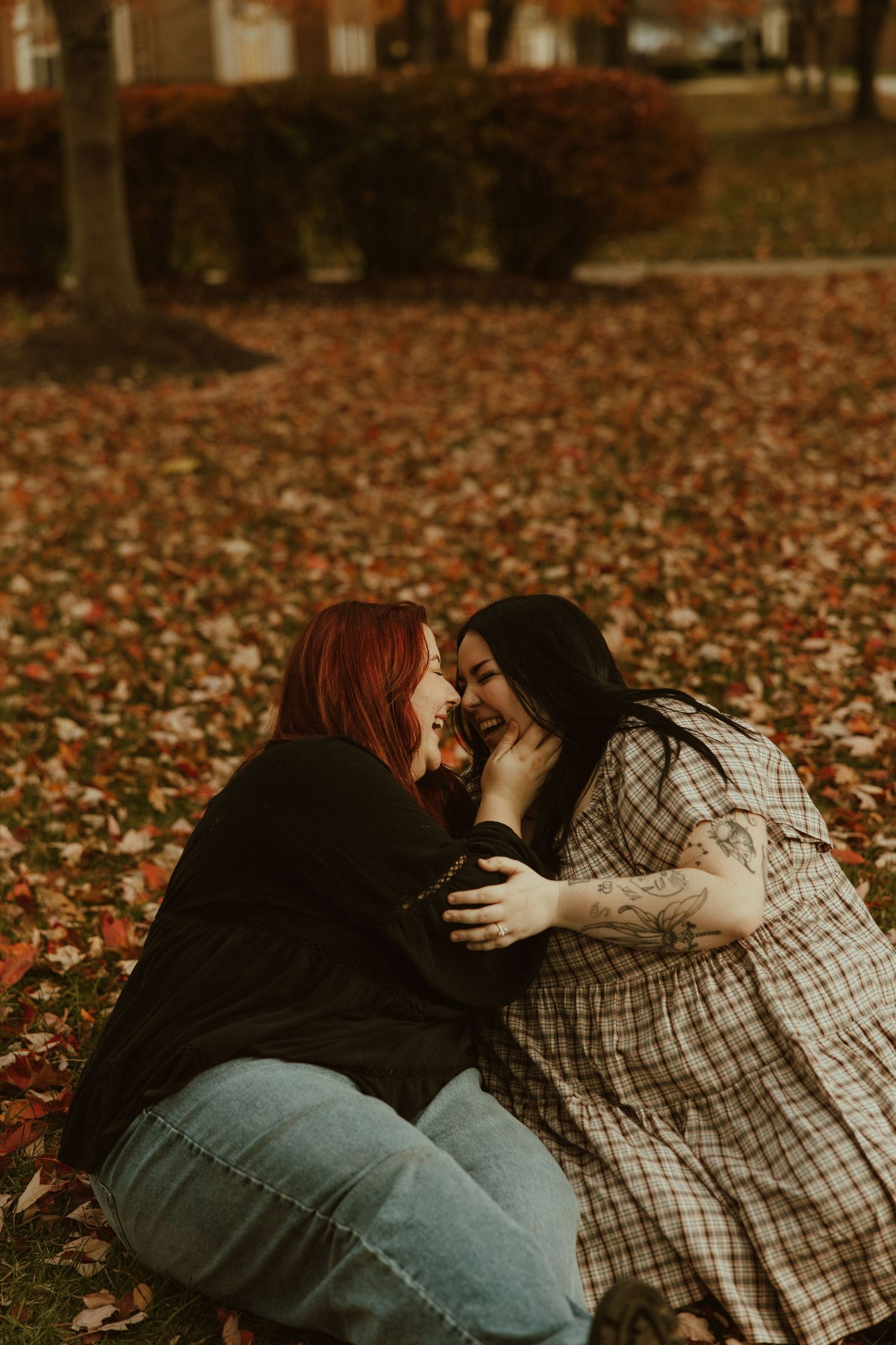 Two people share an intimate moment while sitting together on autumn leaves in a park during golden hour.