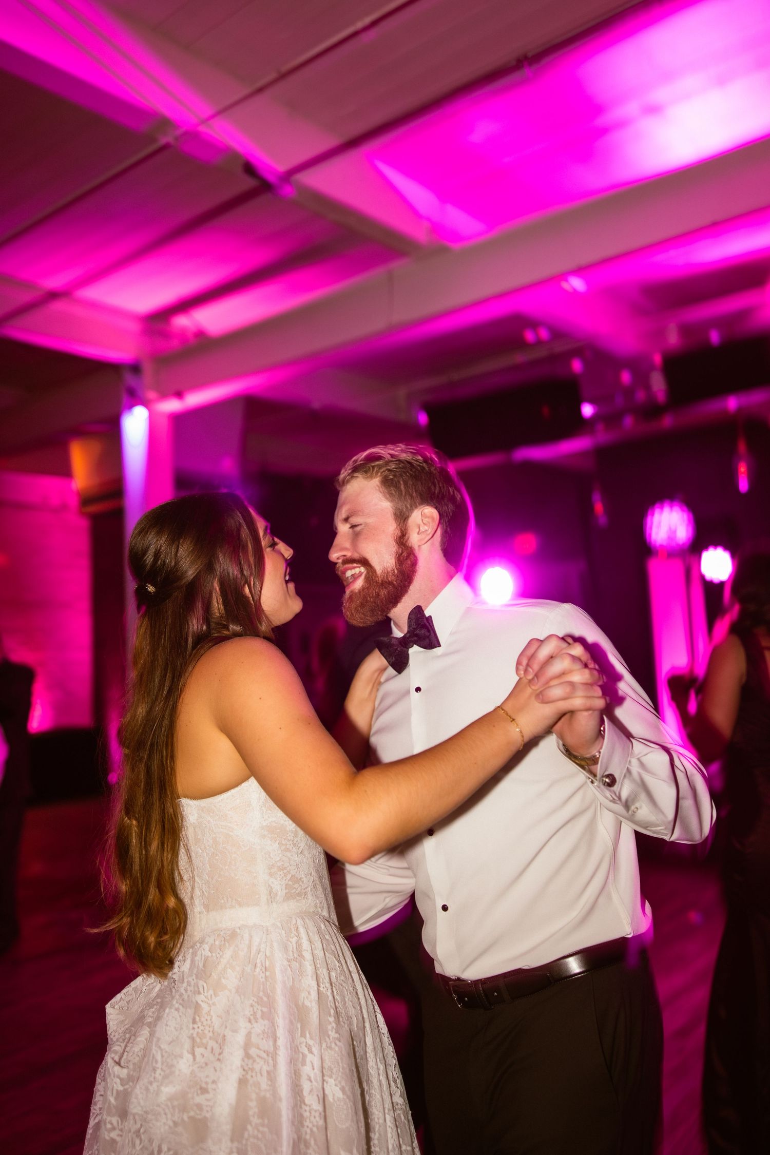 Couple sharing a romantic dance under vibrant pink lighting at their wedding reception.