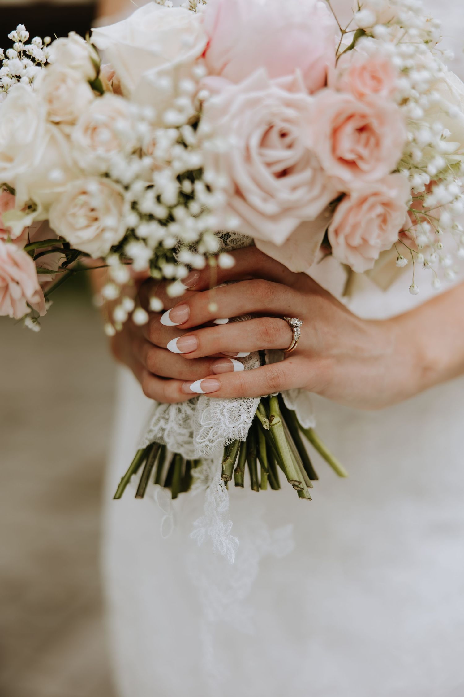 Delicate pink and white wedding bouquet with roses and baby's breath held by hands wearing an engagement ring.