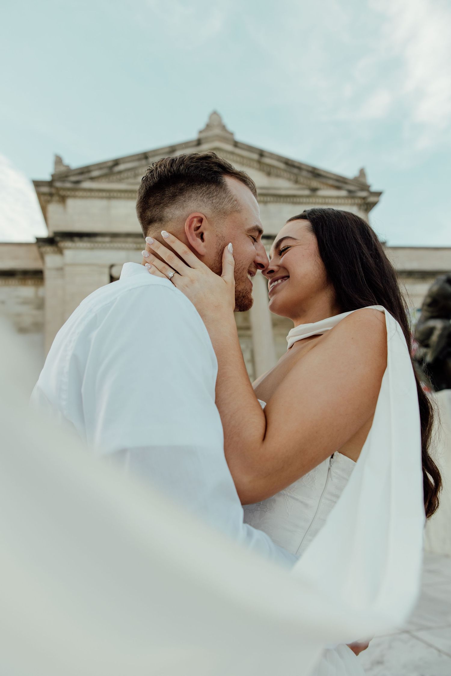 A romantic wedding couple shares intimate moments in front of a grand historic building with white columns.