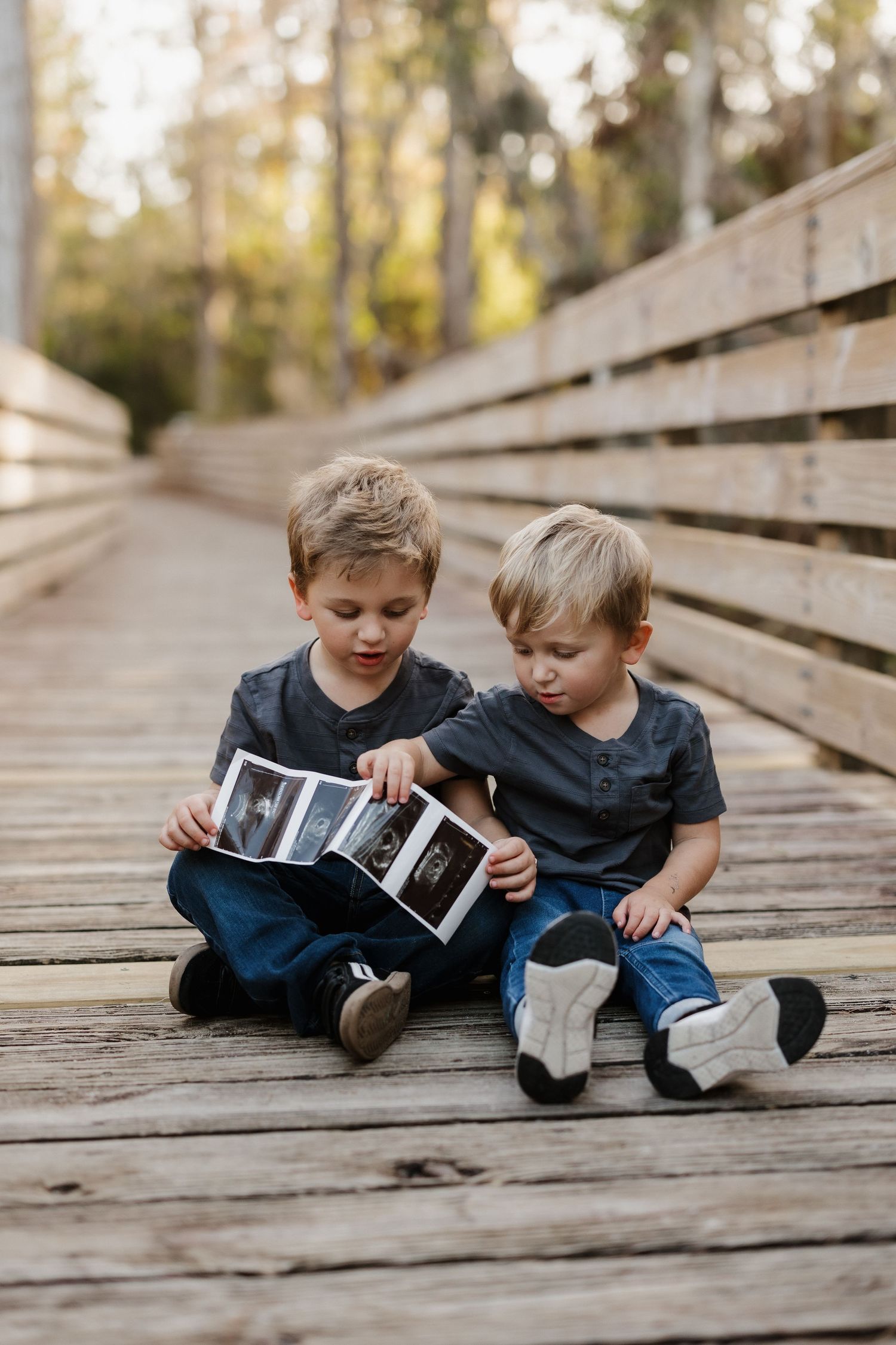 Two young boys sitting on wooden bridge examining ultrasound photos.